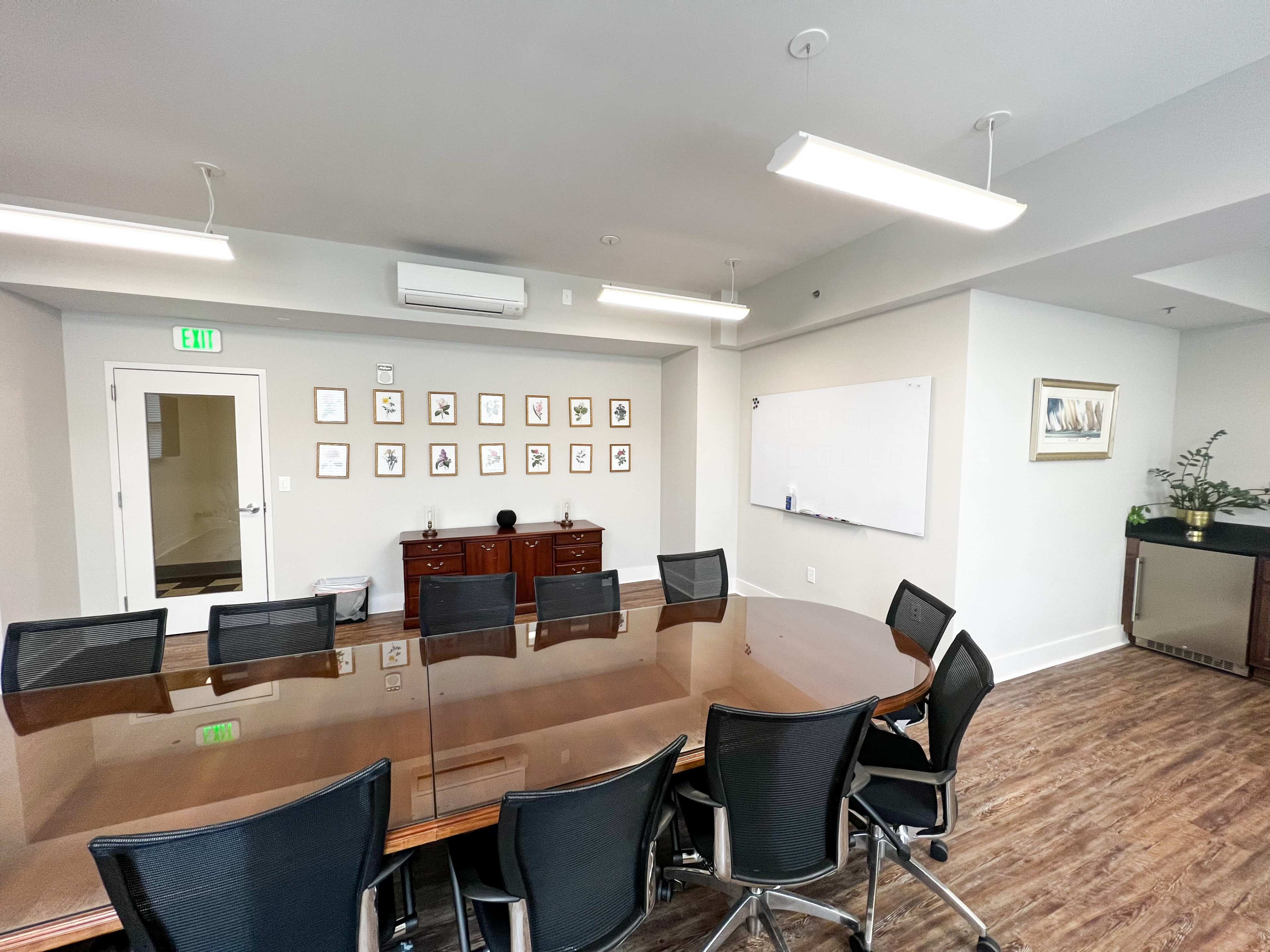 A modern conference room with a large table surrounded by black ergonomic chairs, a whiteboard on one wall, and framed pictures displayed on another.