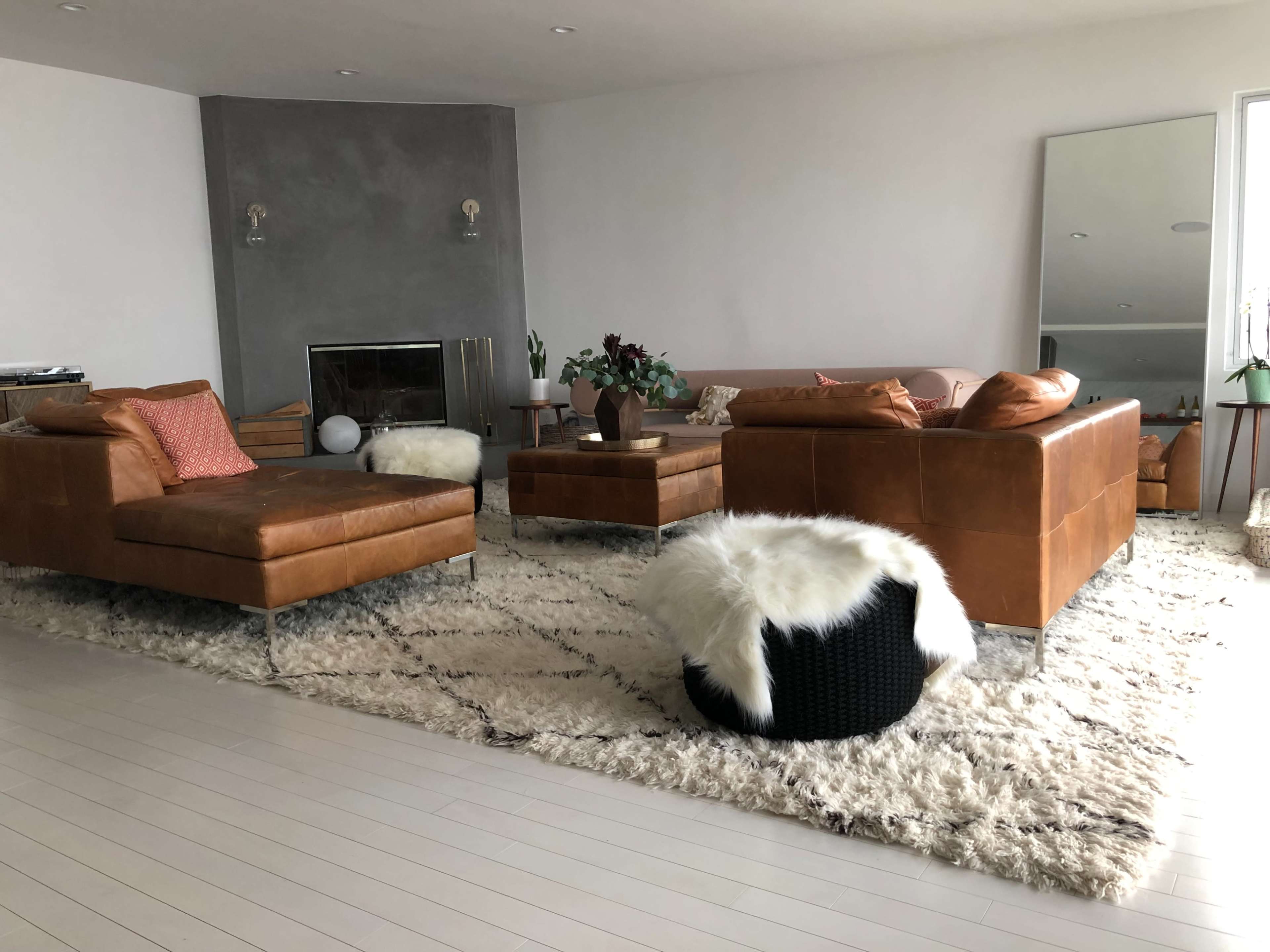 A modern living room with two brown leather sofas, a shaggy rug, a coffee table, and a large mirror against the wall.