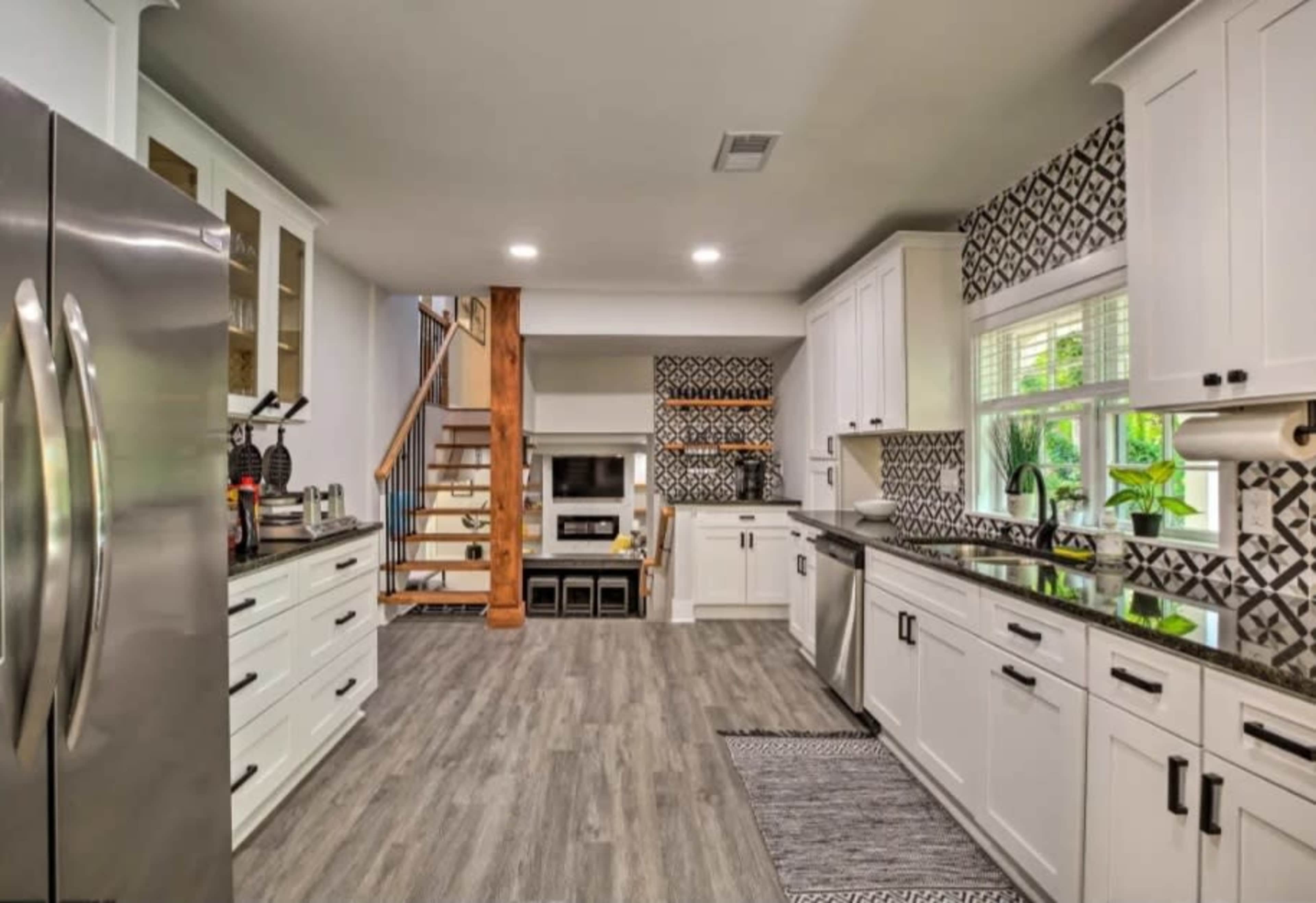 A modern kitchen with white cabinets, stainless steel appliances, and a patterned backsplash, featuring an open layout that connects to a staircase and living area.