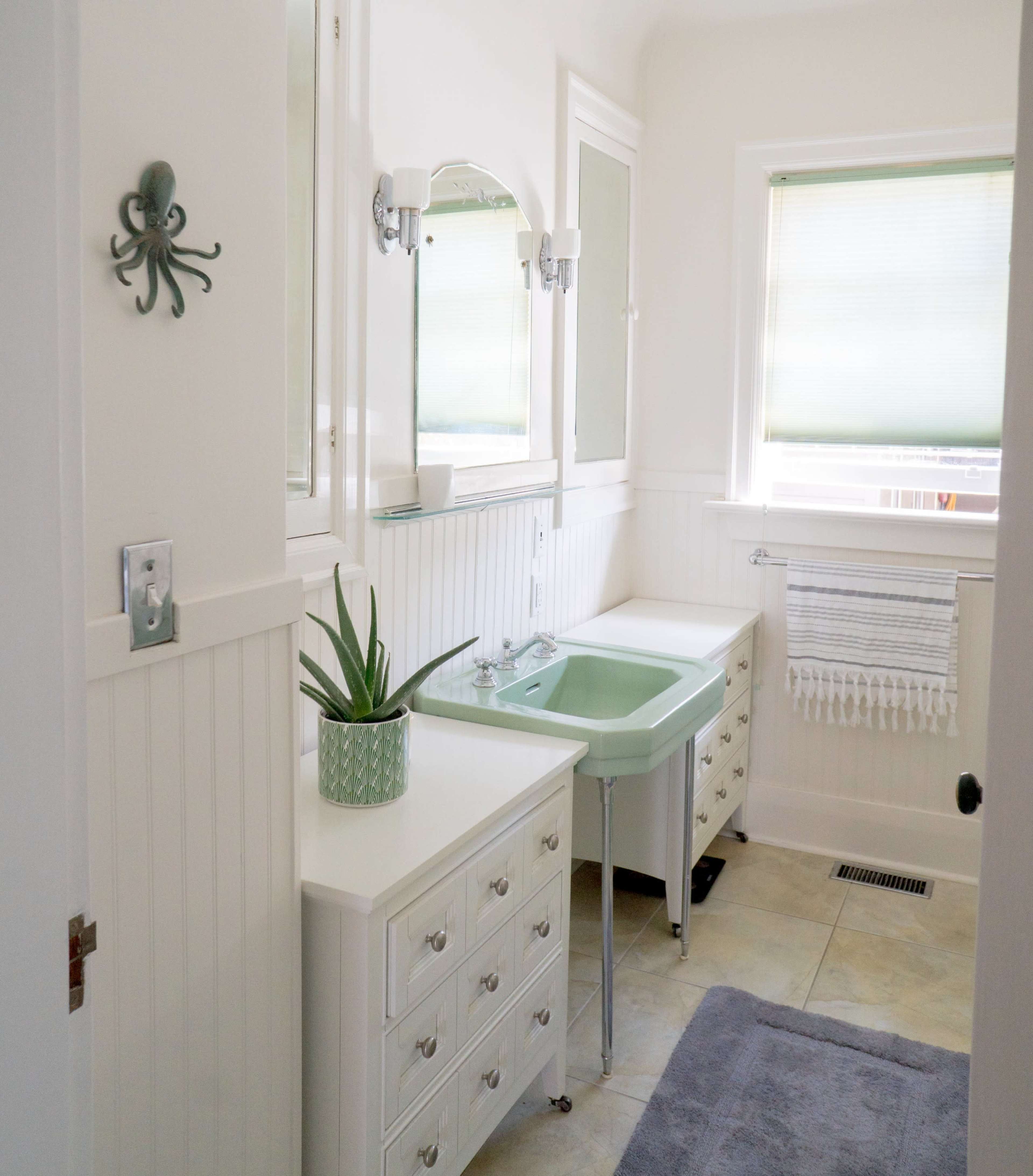 A bright bathroom features a mint green sink, white cabinetry, a wall-mounted mirror, and an octopus decoration.