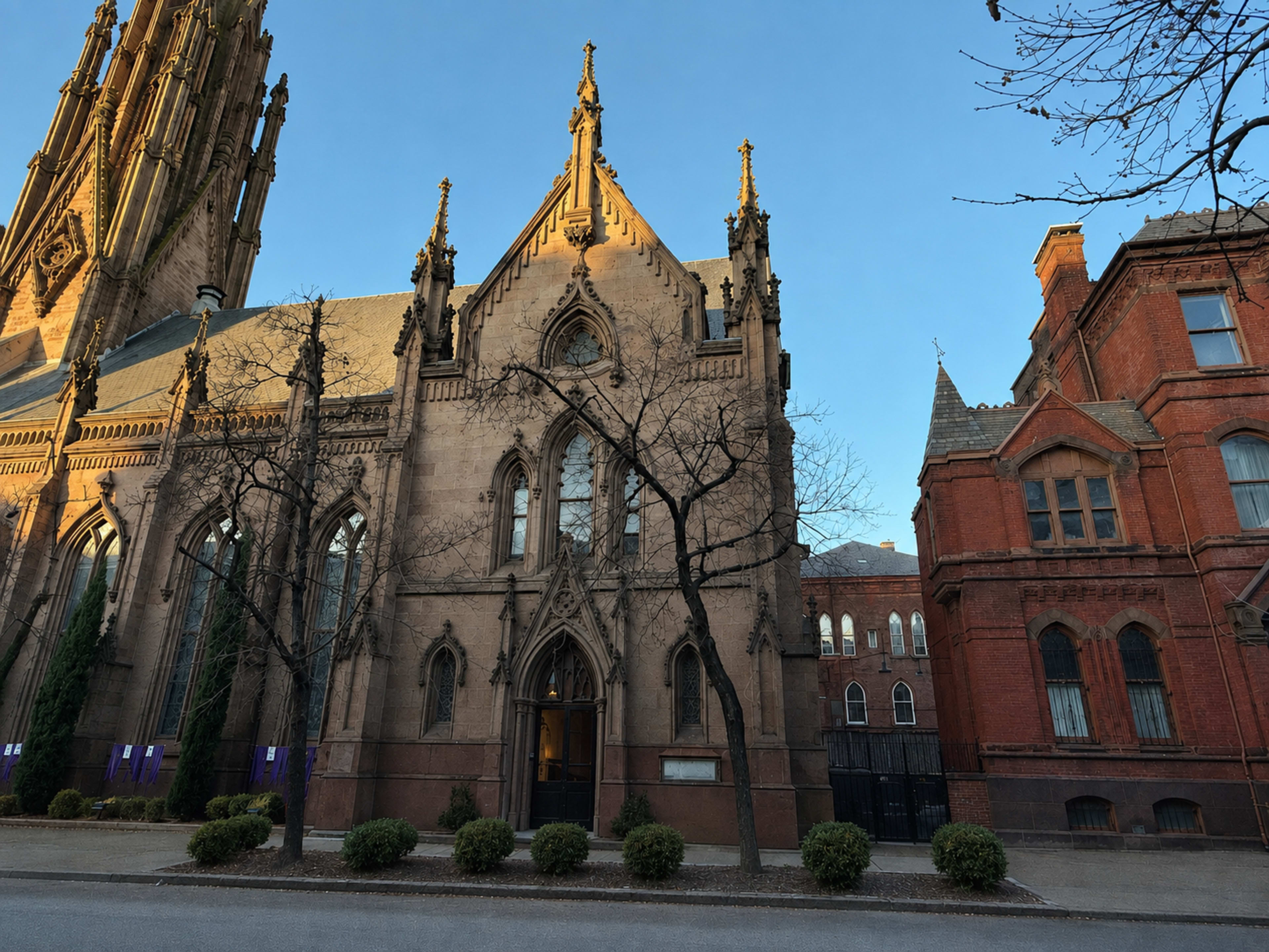 The image shows a tall Gothic church with intricate architectural details alongside a brick building, set against a clear sky.