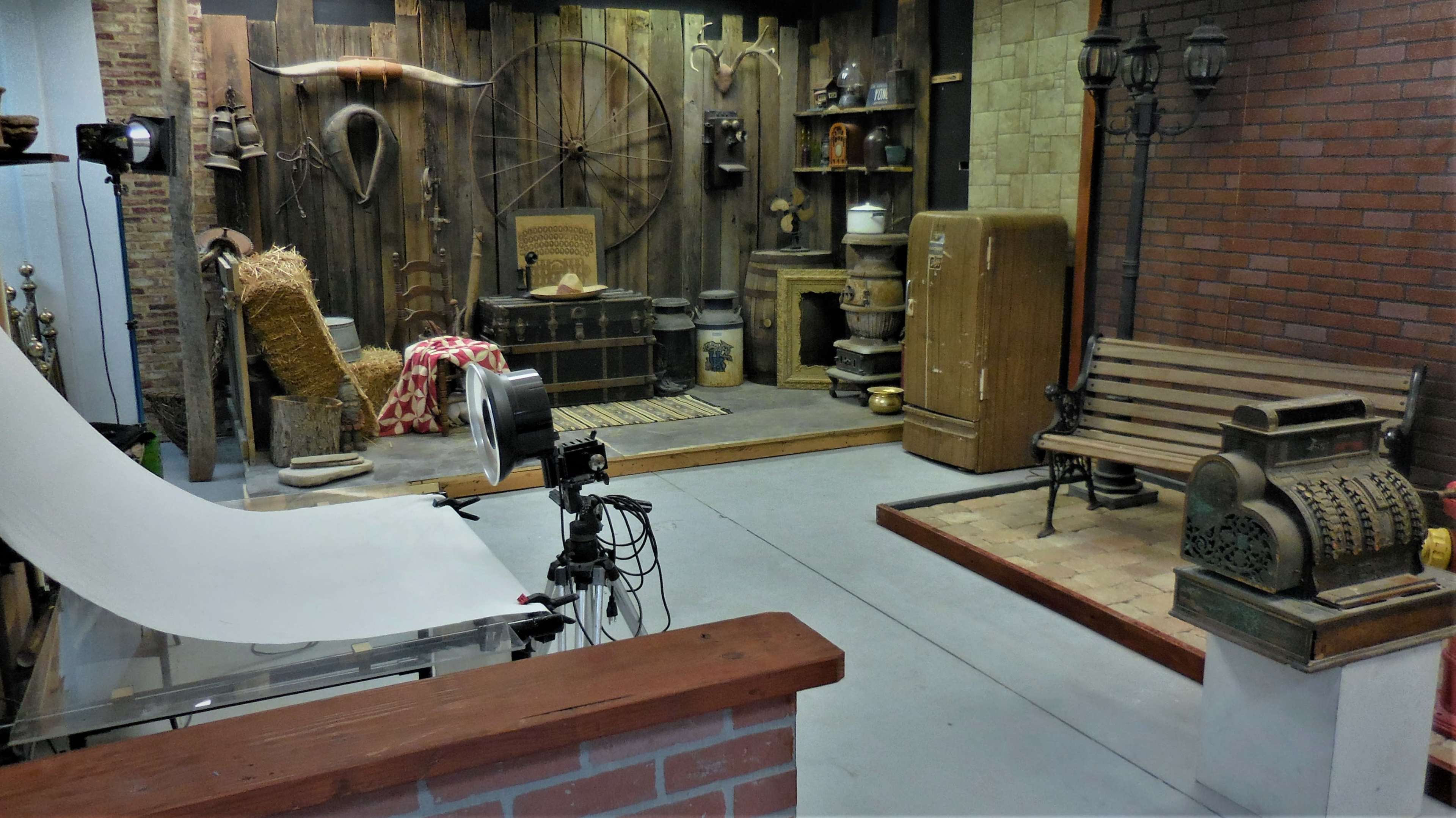 A vintage-themed room featuring various historical items, including a wooden bench, an antique cash register, and decorative objects arranged against a rustic wall.