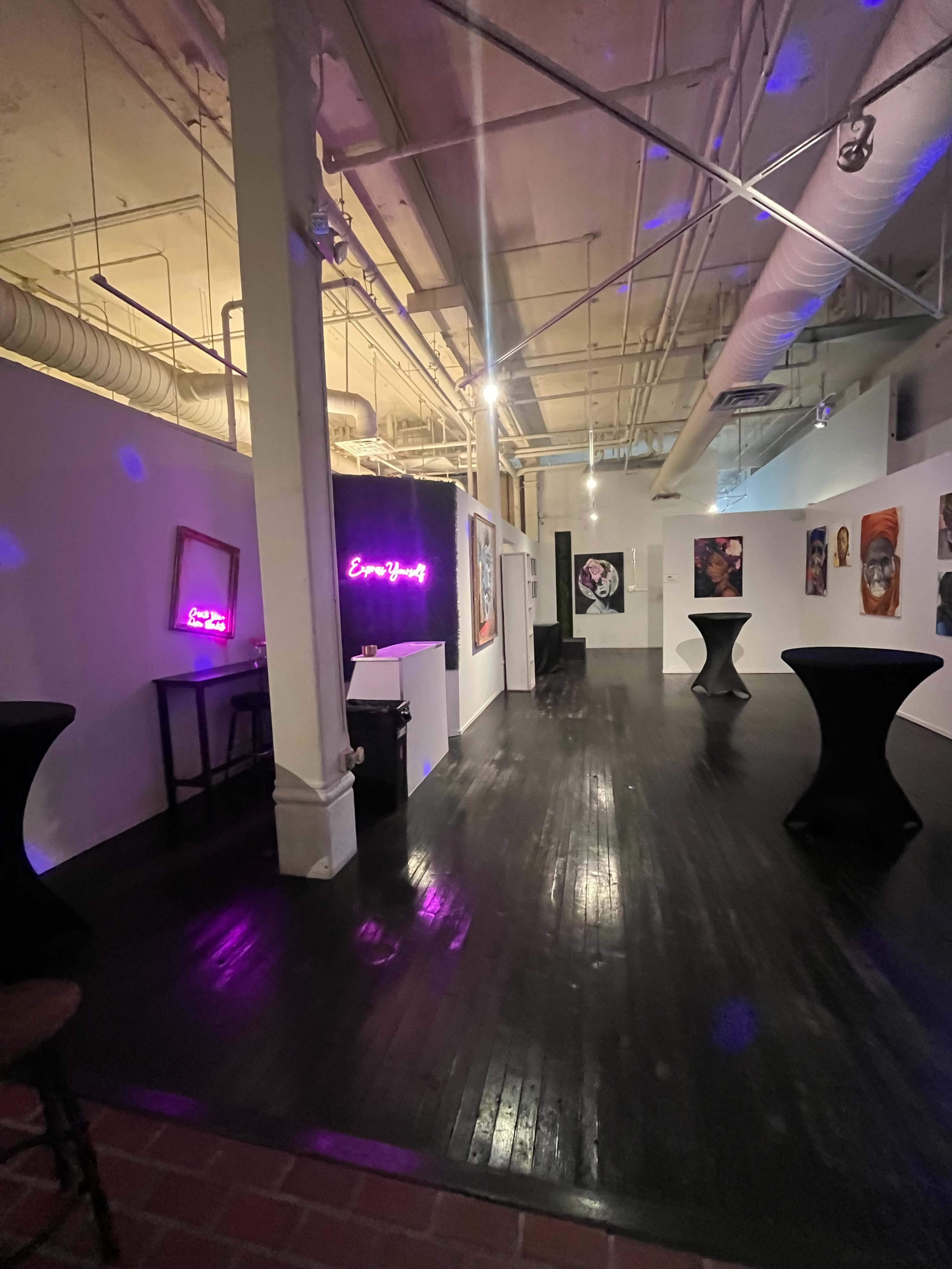 The image shows an art gallery with various artworks displayed on white walls and illuminated by purple lighting.