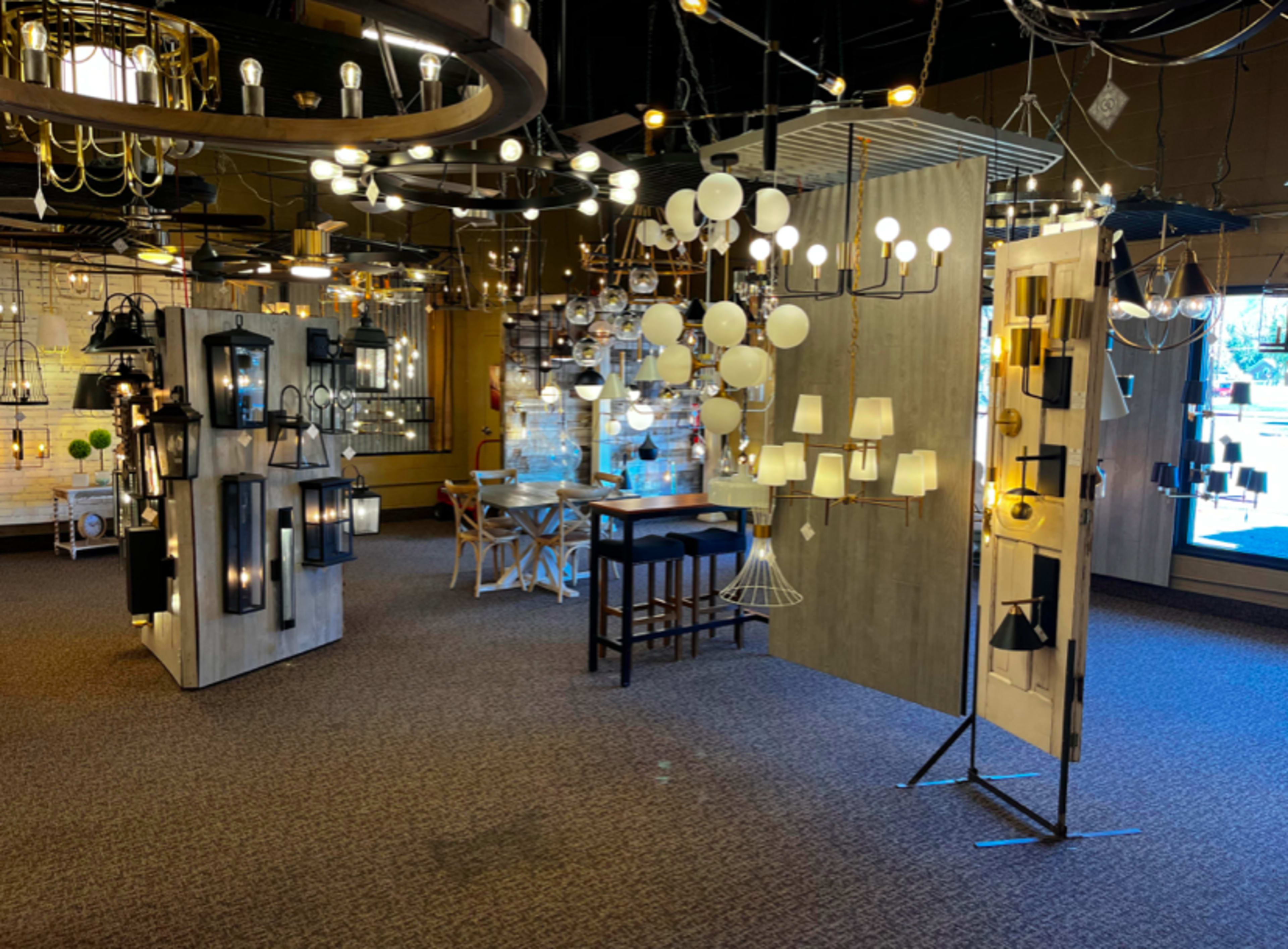 An interior display room filled with various lighting fixtures arranged on stands and walls, with a seating area in the center.