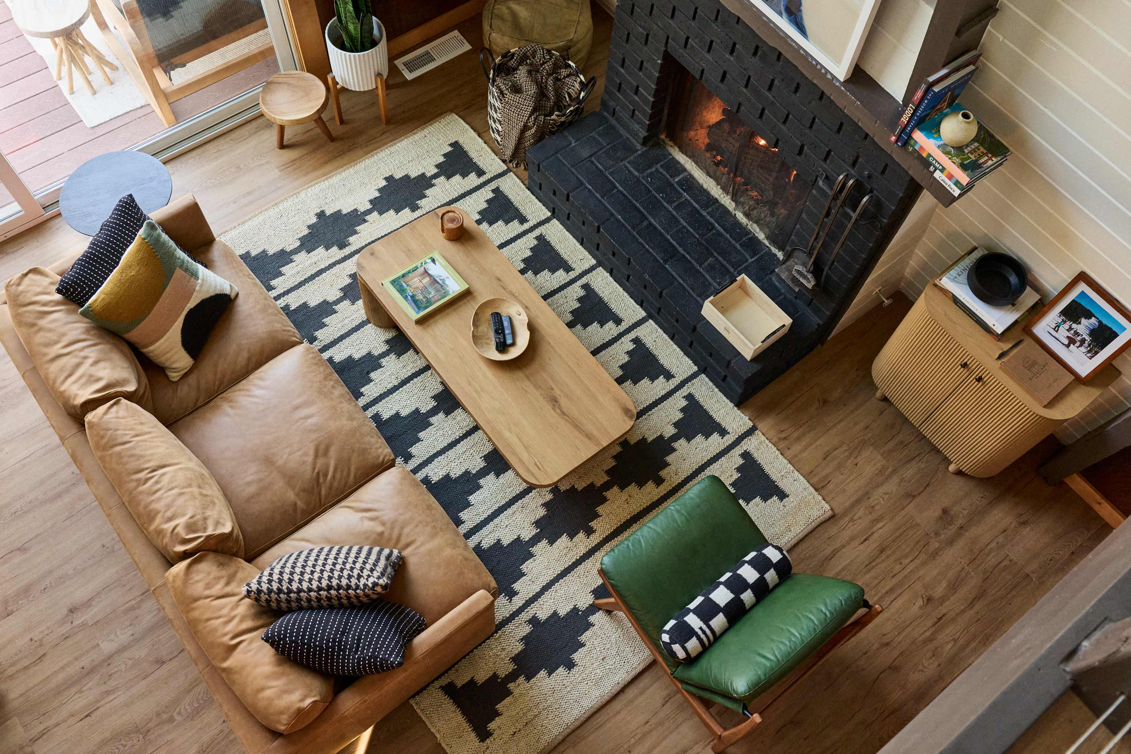The image shows a cozy living room featuring a leather sofa, a wooden coffee table, an area rug with a geometric pattern, and a black fireplace.