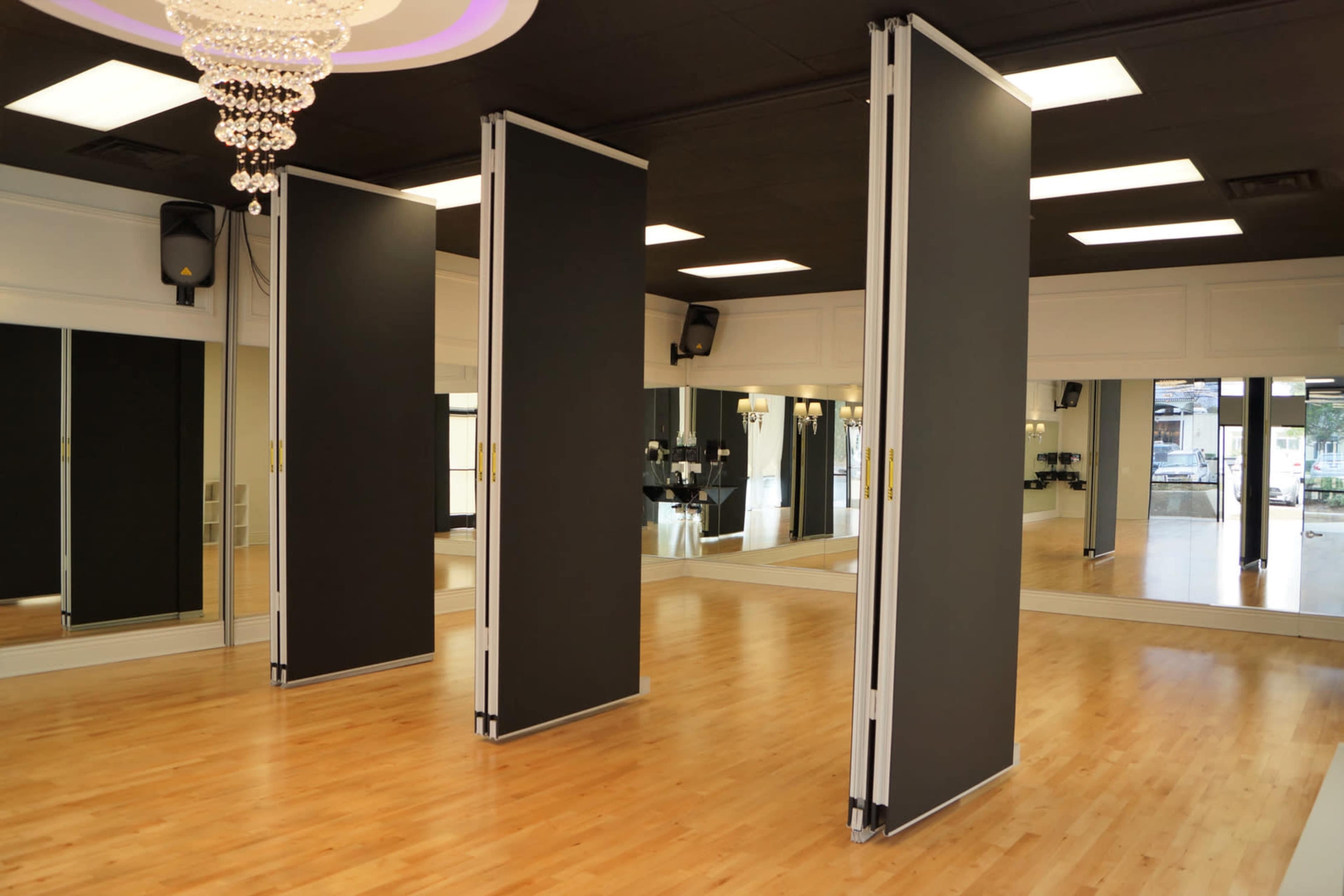 A dance studio with wooden flooring, mirrored walls, and three movable partition screens.