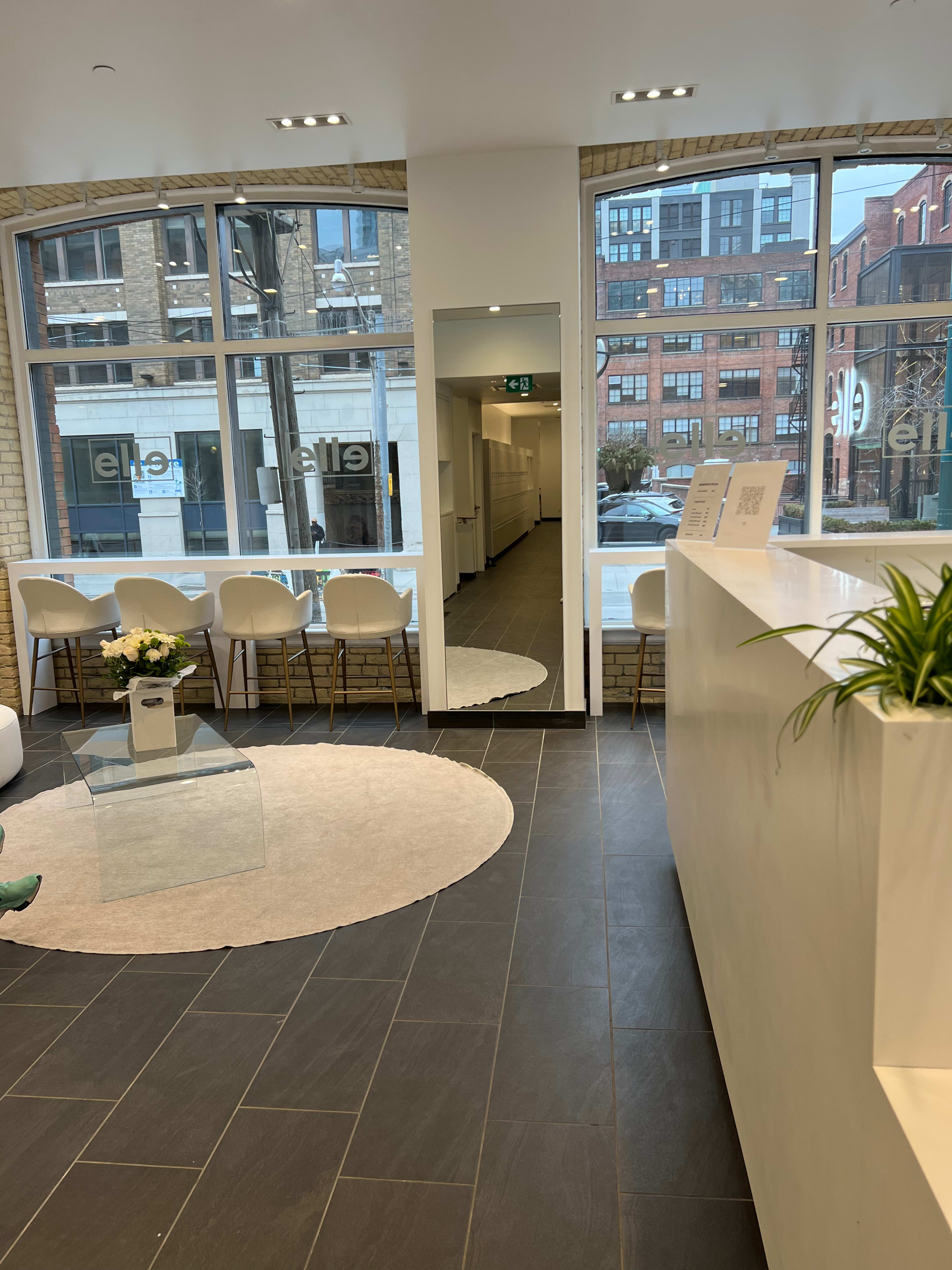 A modern reception area featuring a circular mirror, white furniture, and a light-colored rug, with large windows displaying a cityscape outside.