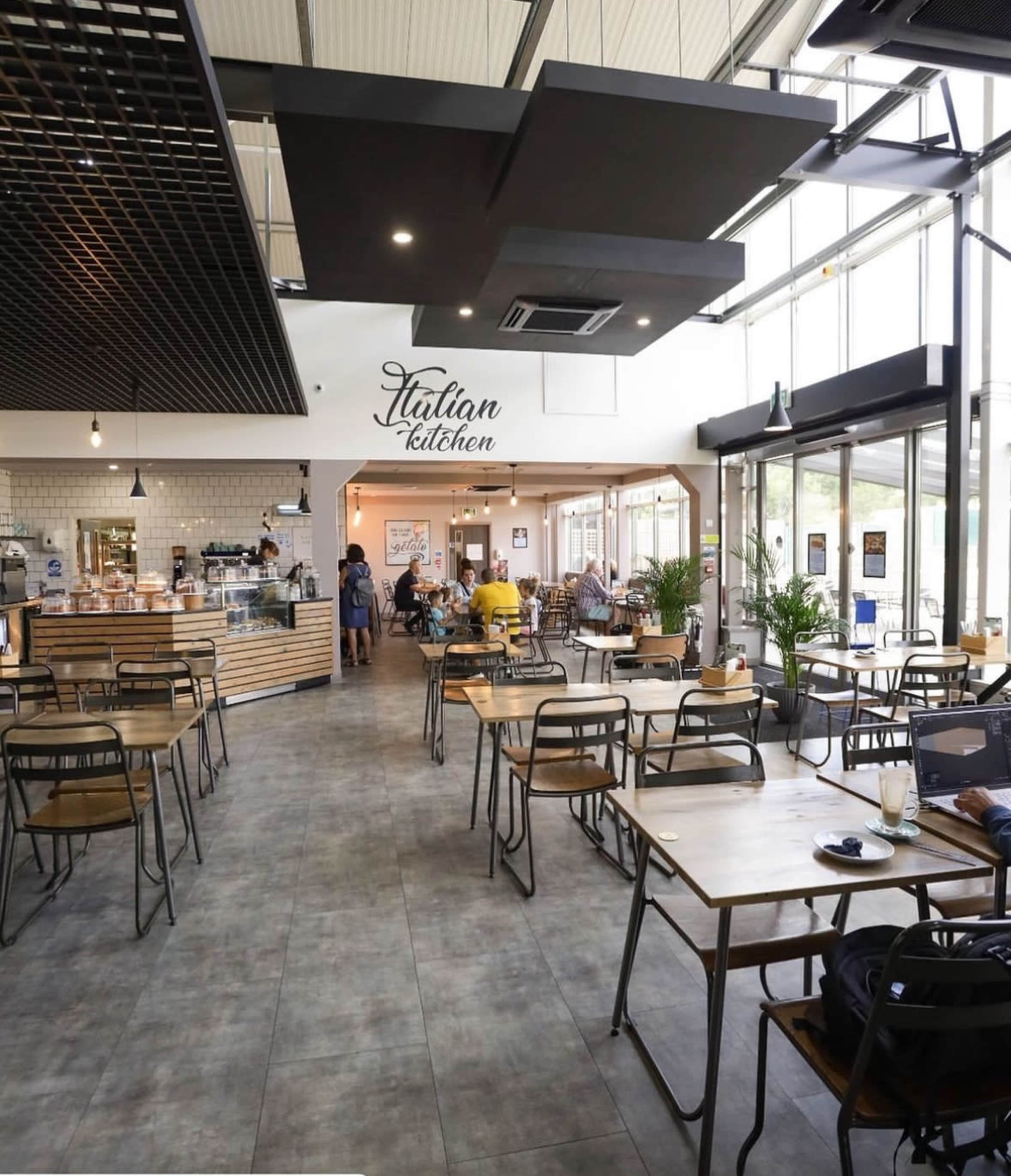 A modern Italian kitchen cafe with tables and chairs arranged along a spacious interior, featuring a counter and a menu display in the background.