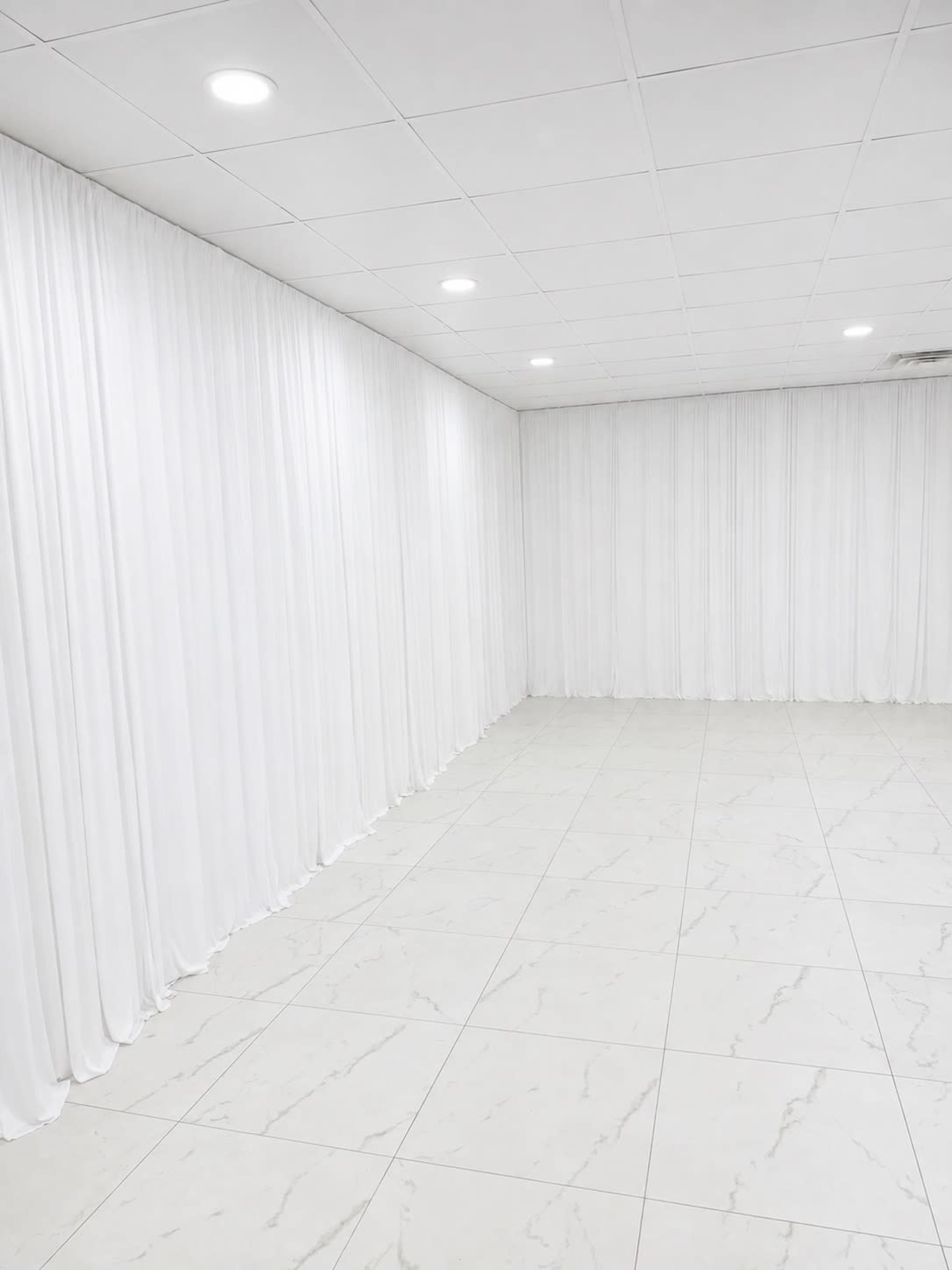 The image shows an empty room with white draped curtains and a glossy tiled floor.