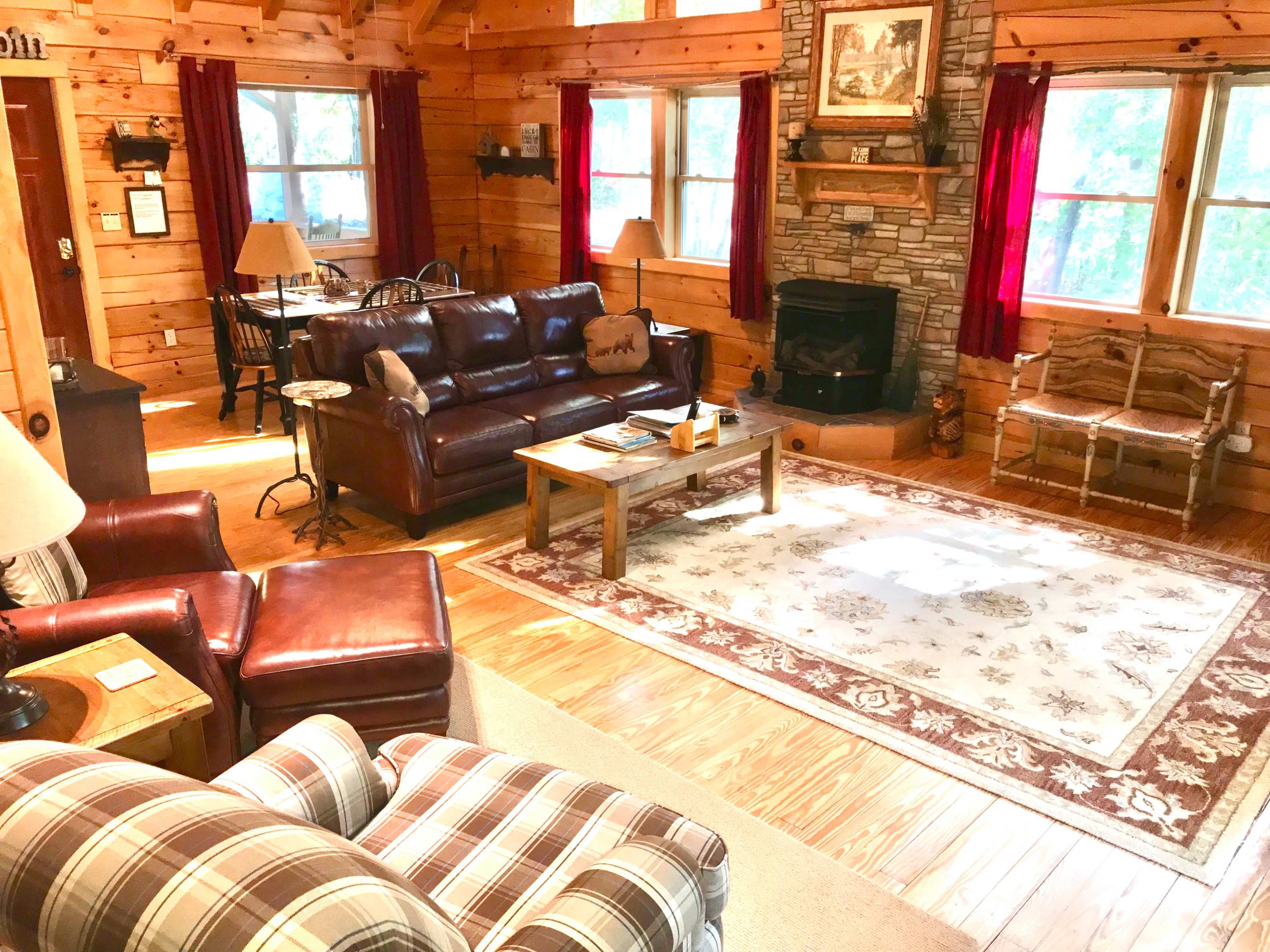 A cozy log cabin living room with wooden walls, a stone fireplace, and a combination of leather and fabric seating.