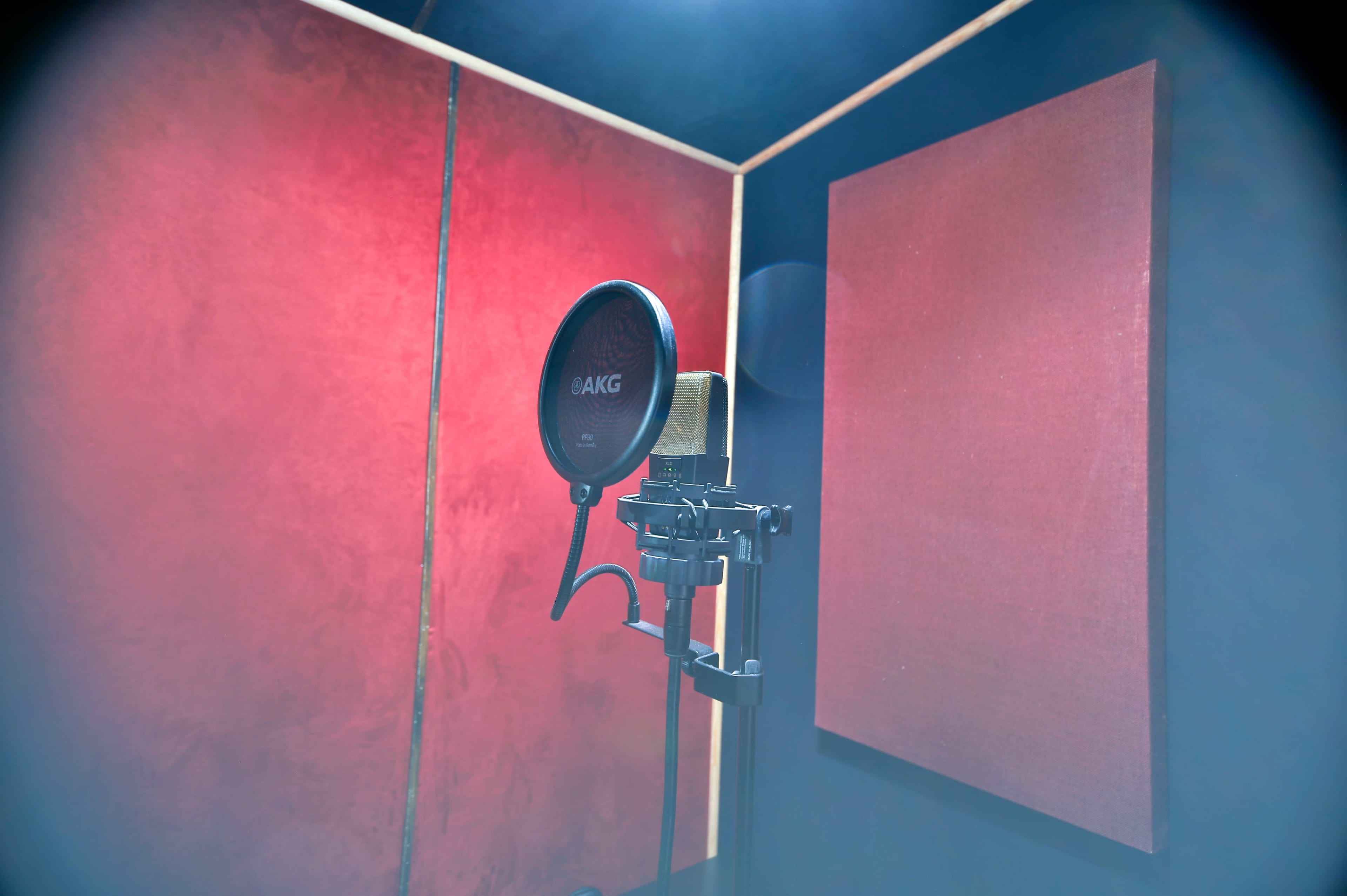 A microphone is positioned on a stand in a soundproof recording studio with red walls.