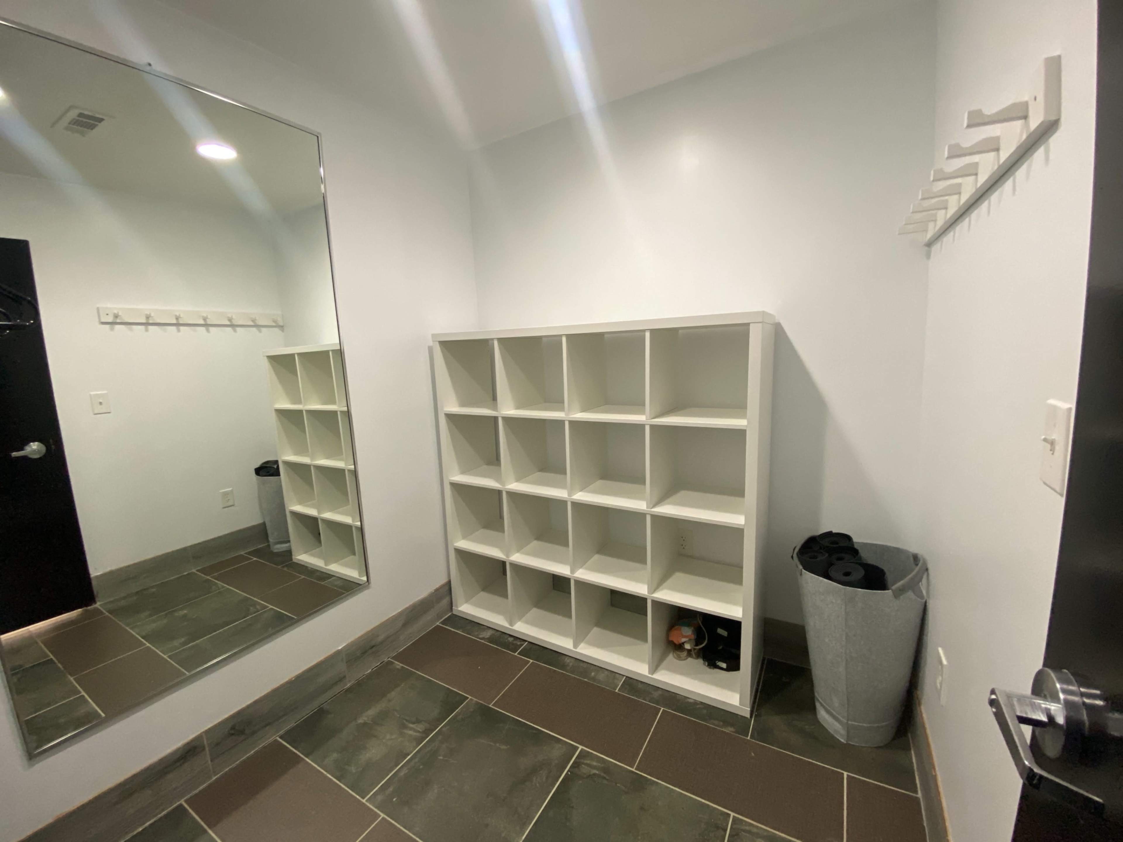A minimalist entryway with a large mirror, a cubical shelving unit, a trash can, and a wall-mounted rack for hanging items.