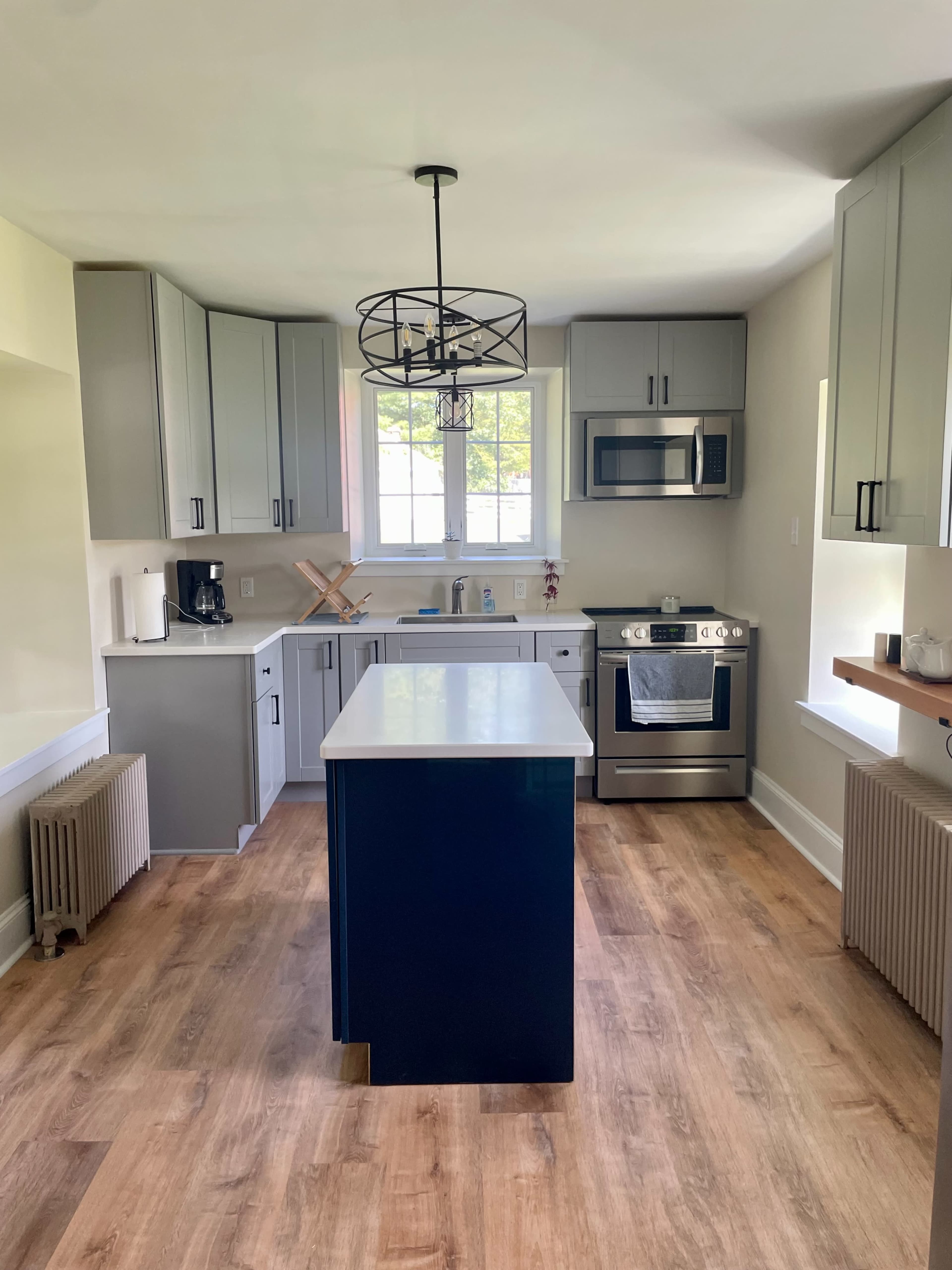 A modern kitchen features gray cabinets, a navy blue island, stainless steel appliances, and hardwood flooring.
