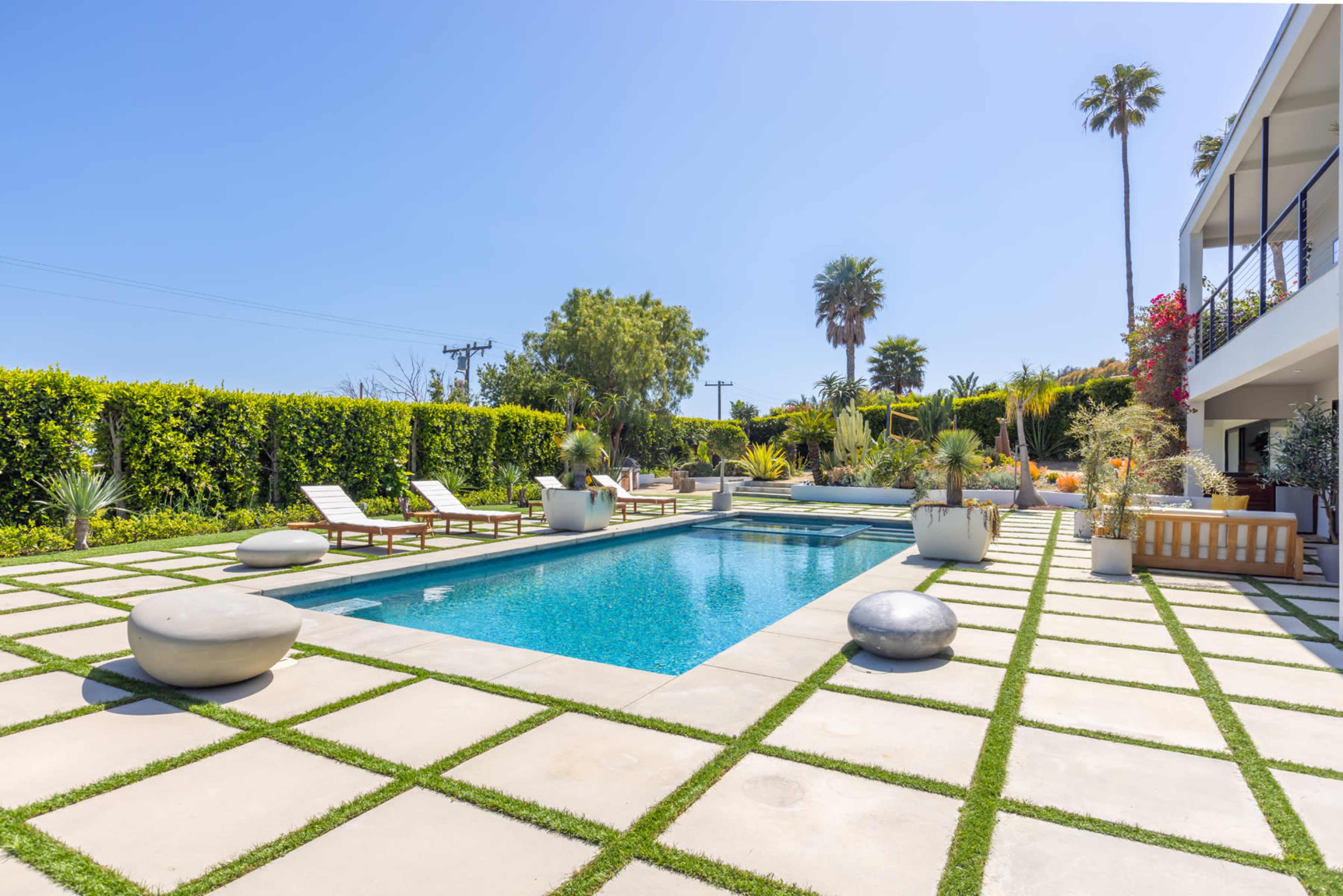 A modern backyard with a swimming pool surrounded by lounge chairs, decorative stones, and well-maintained landscaping.