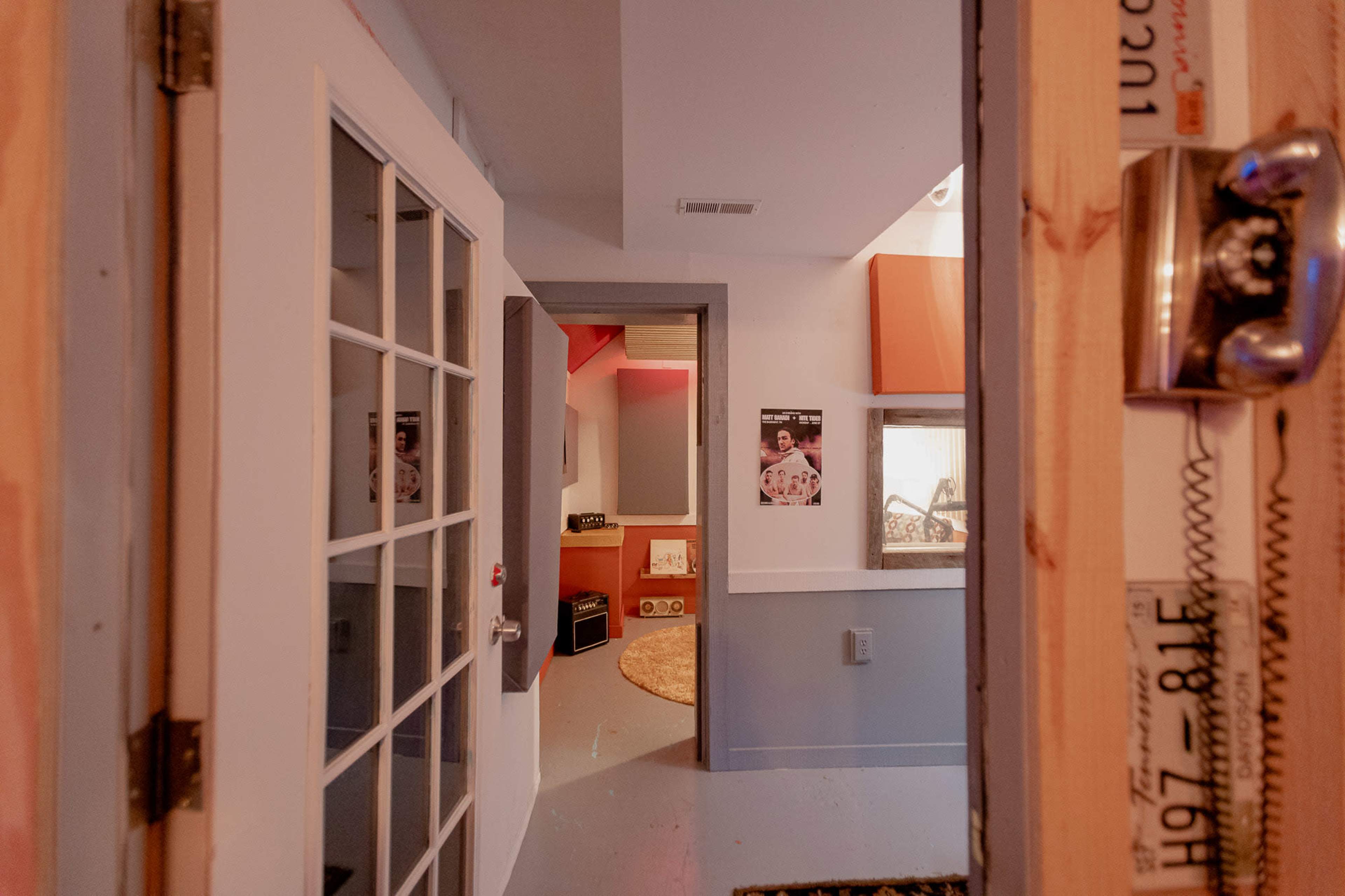 A doorway leading into a hallway with light-colored walls, a circular rug, and posters on the walls.