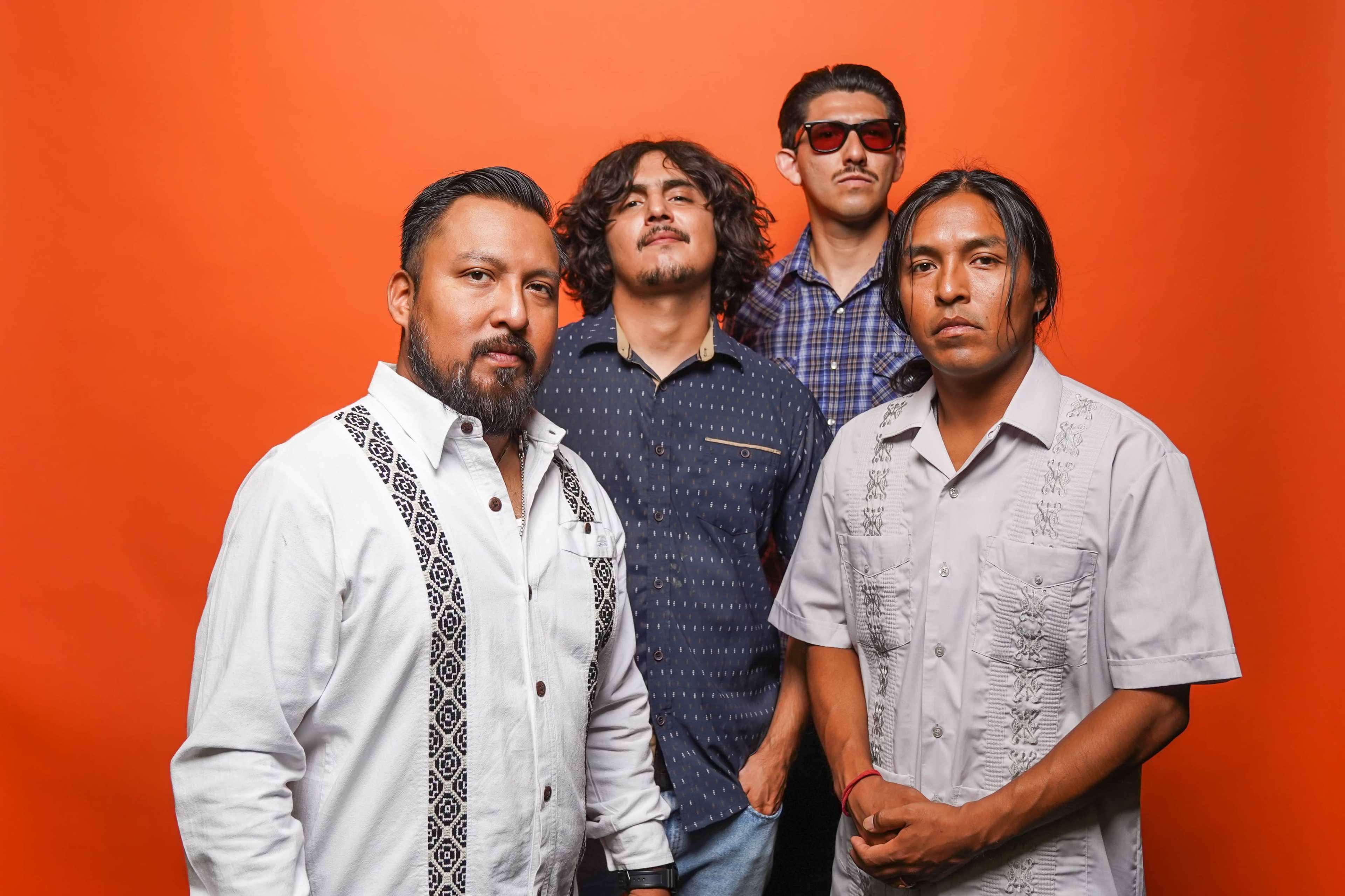 Four men stand together, posing in front of a bright orange background.