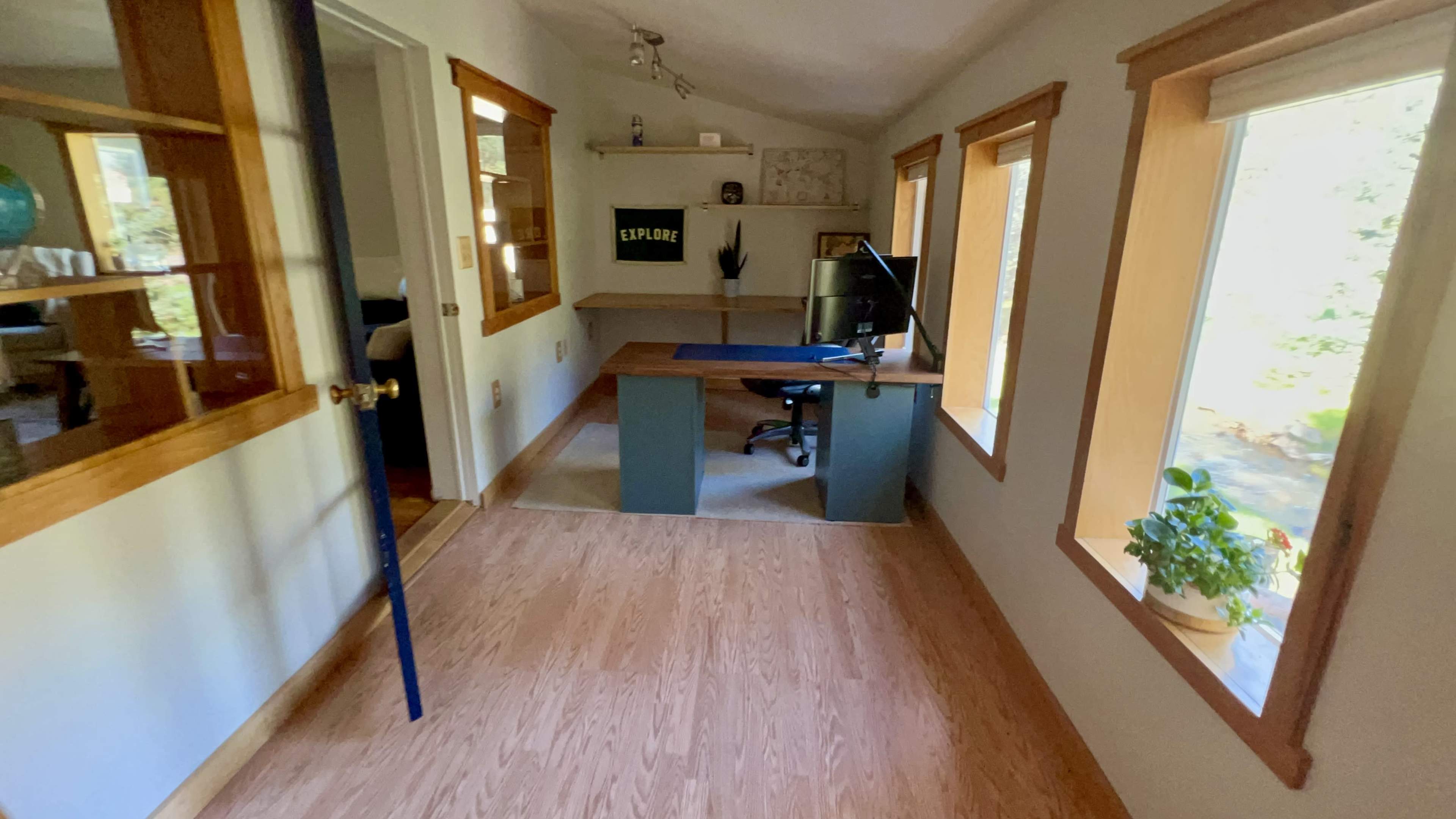 A small home office with a desk and chair, illuminated by natural light from the windows.