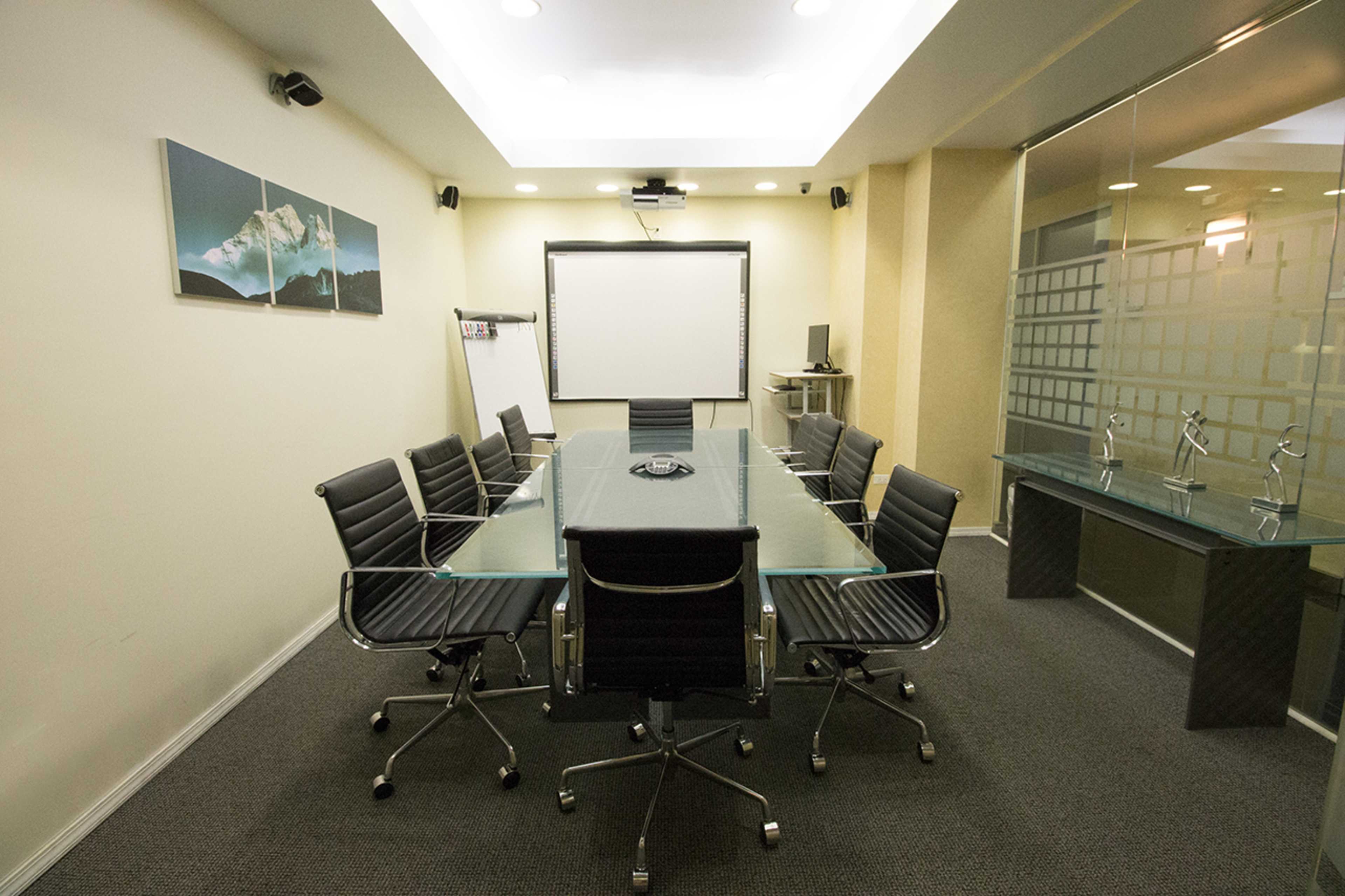 The image shows a modern conference room with a glass table surrounded by black office chairs, a projection screen, and a whiteboard.