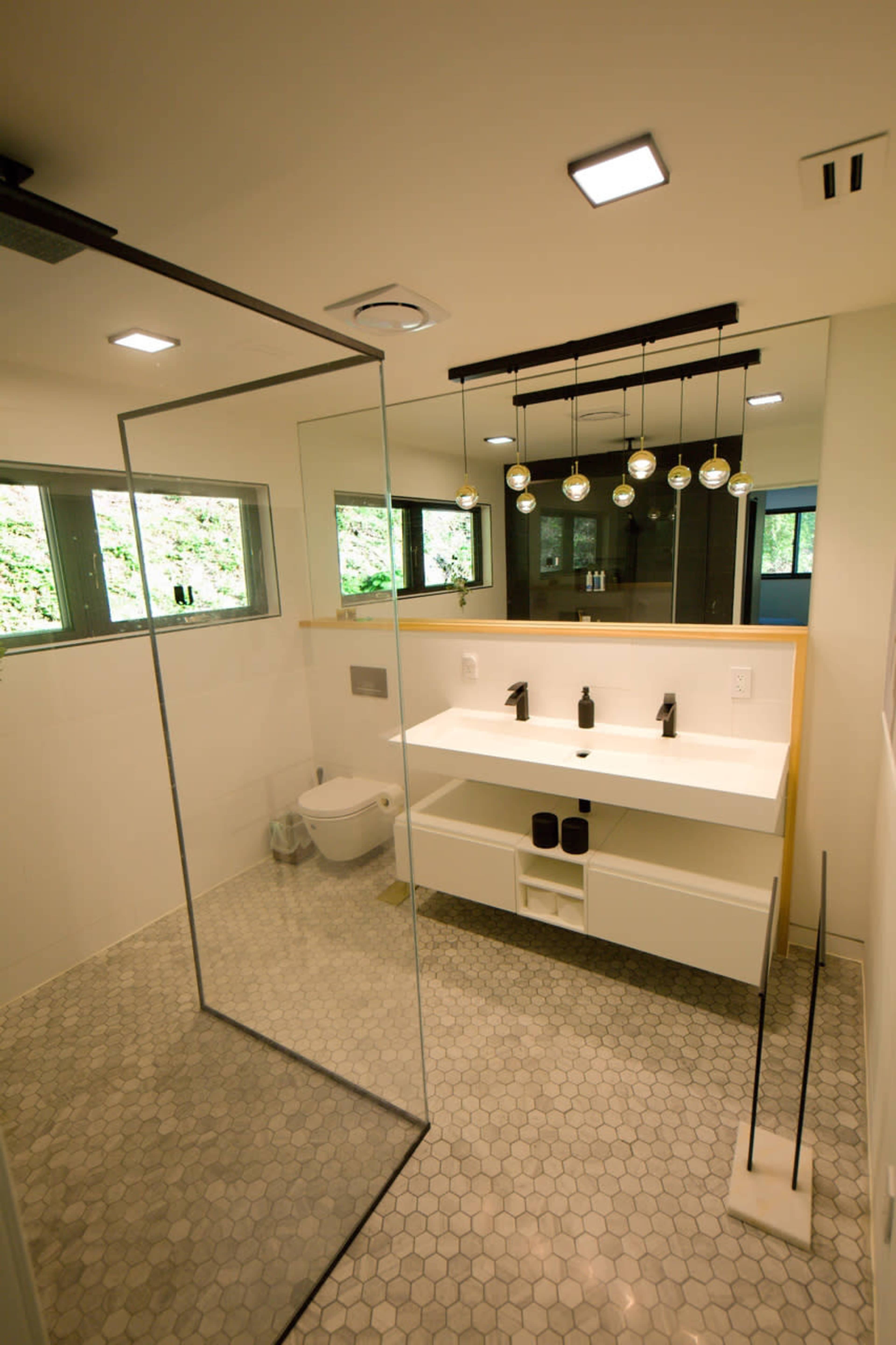 A modern bathroom featuring a glass shower enclosure, a white vanity with two sinks, and hexagonal floor tiles.