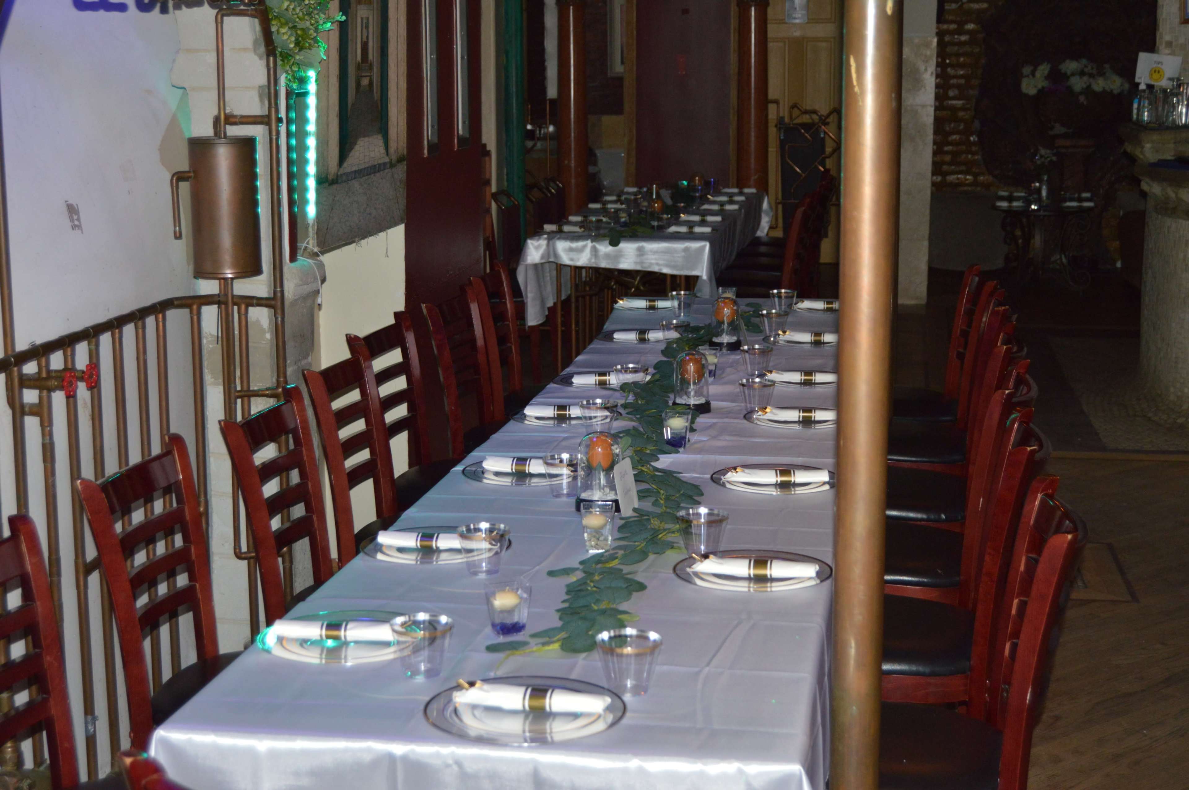A long dining table is set with plates and glasses, surrounded by chairs, in a restaurant's interior.
