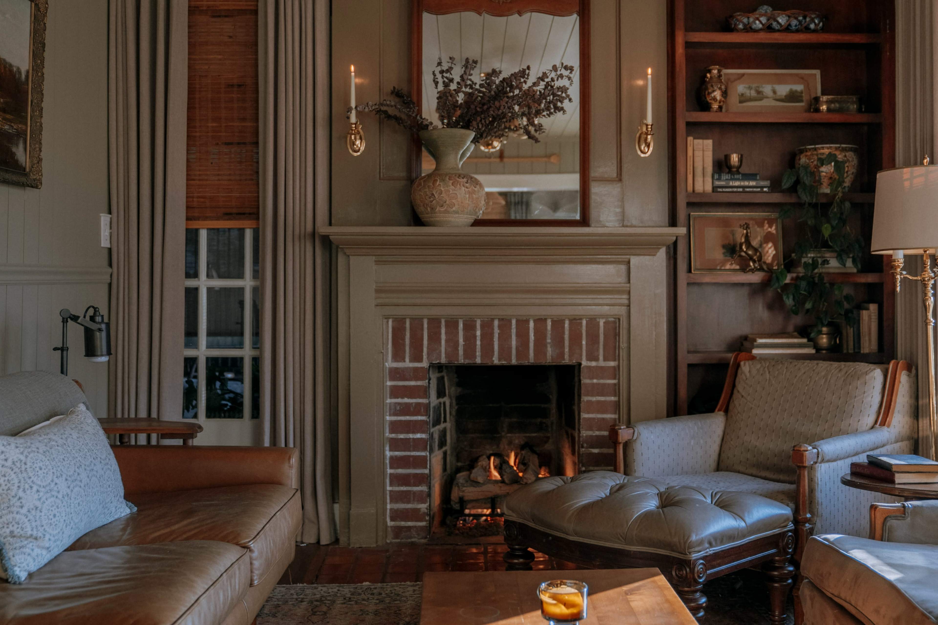 The image depicts a cozy living room featuring a brick fireplace, comfortable seating, and bookshelves adorned with decorative items.