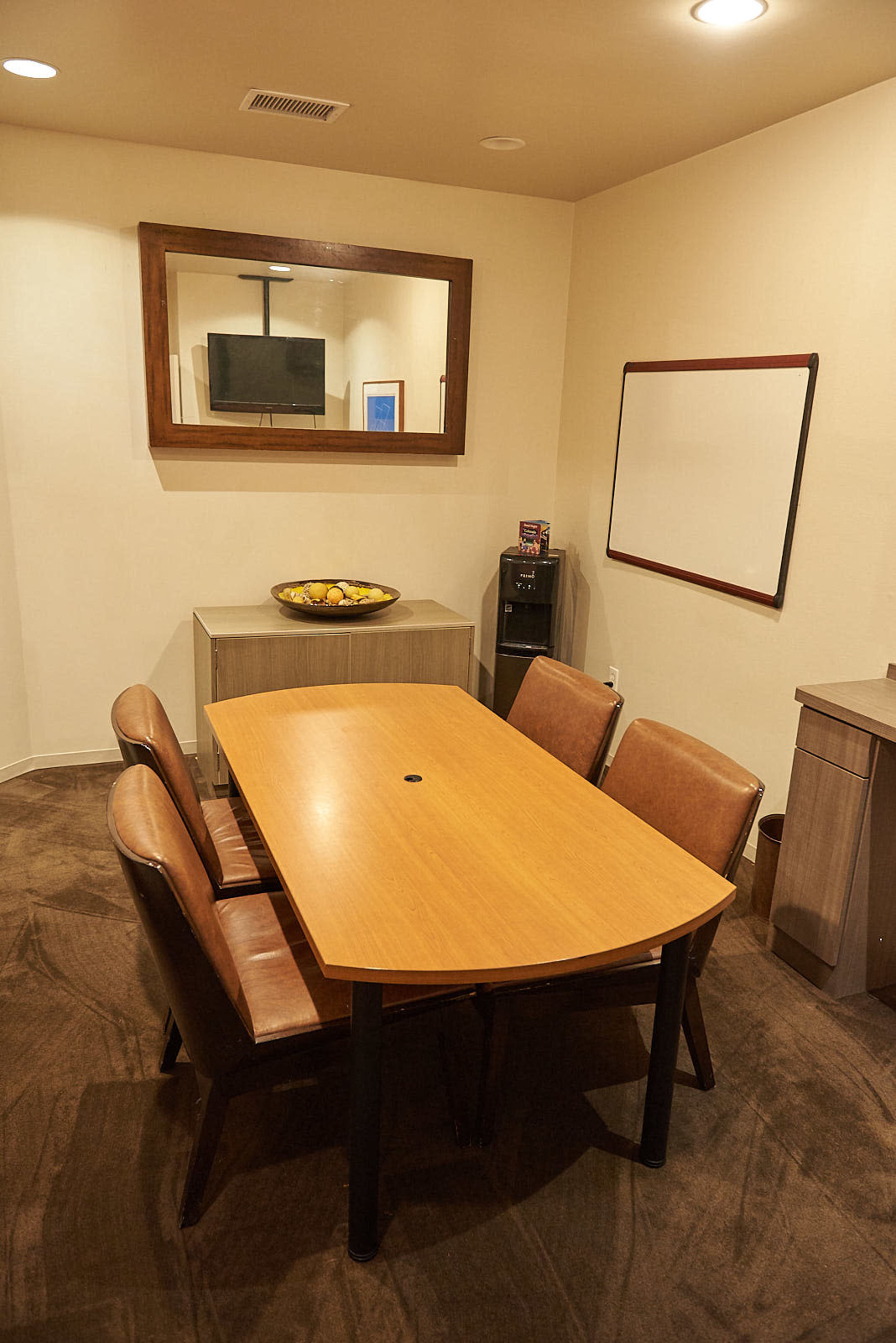 A small conference room is furnished with a wooden table and four leather chairs, featuring a wall-mounted television and a whiteboard.