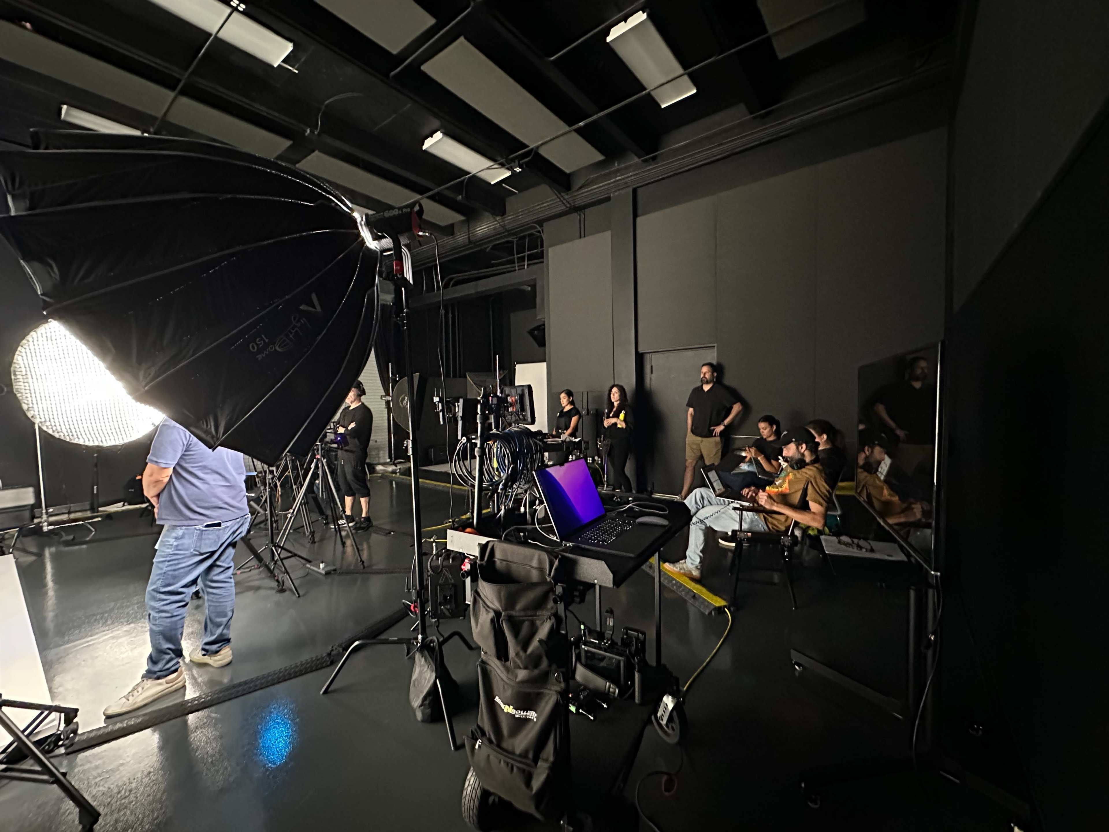 A photography studio setup features multiple lighting equipment and a group of people seated in front of a screen.