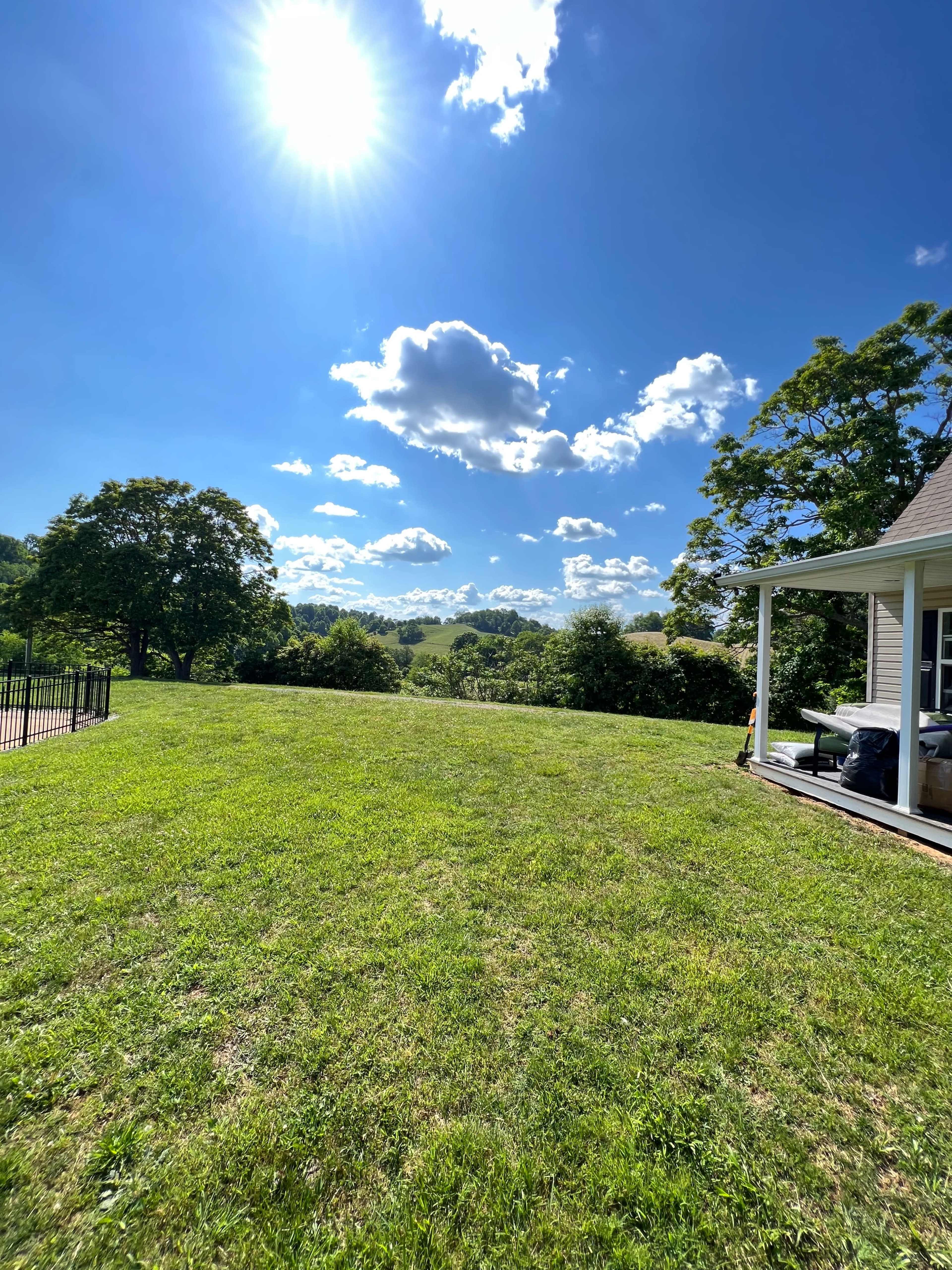 A clear blue sky with scattered clouds overlooks a vast green lawn and distant rolling hills.