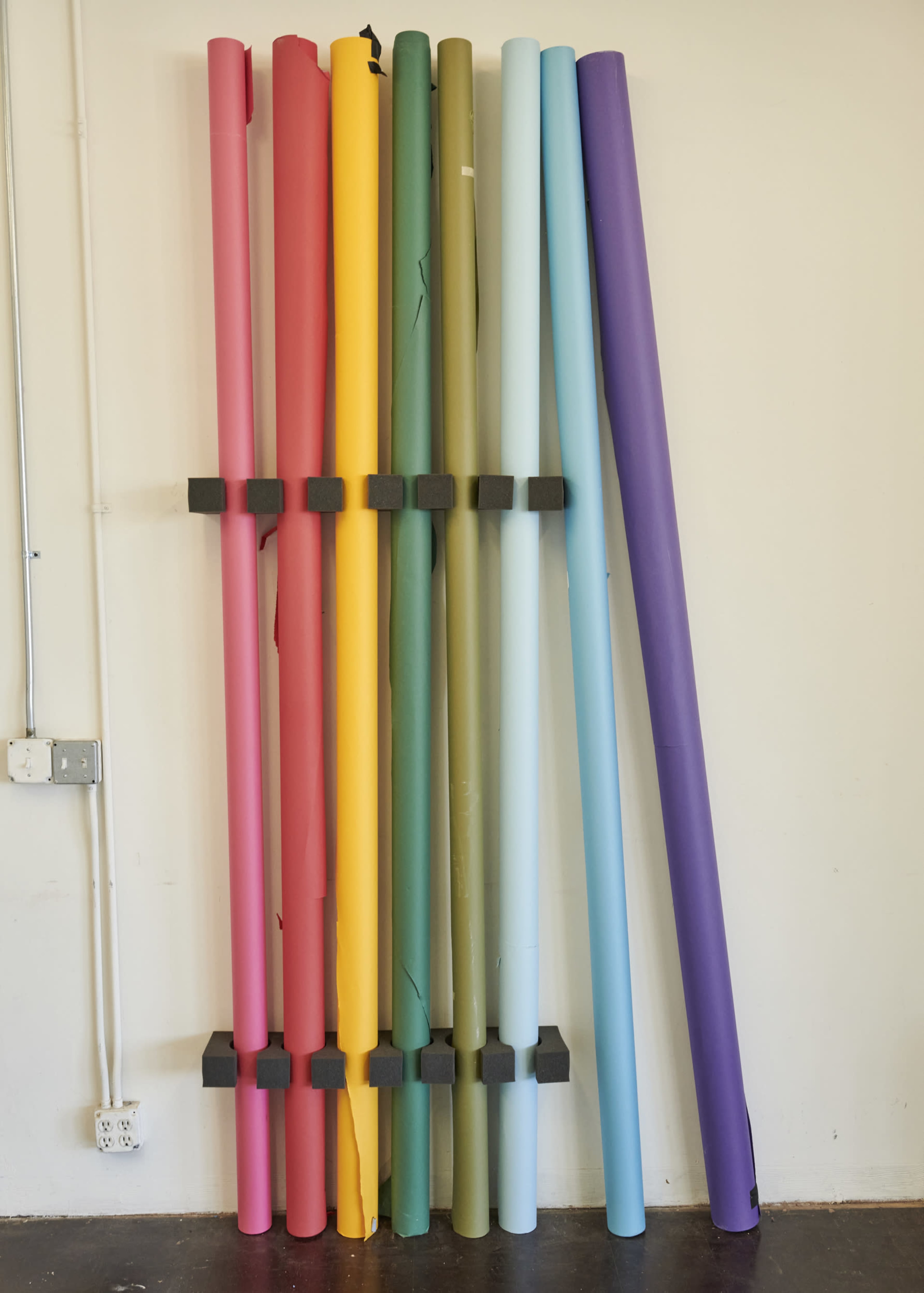 A collection of rolled paper in various colors stacked against a wall.