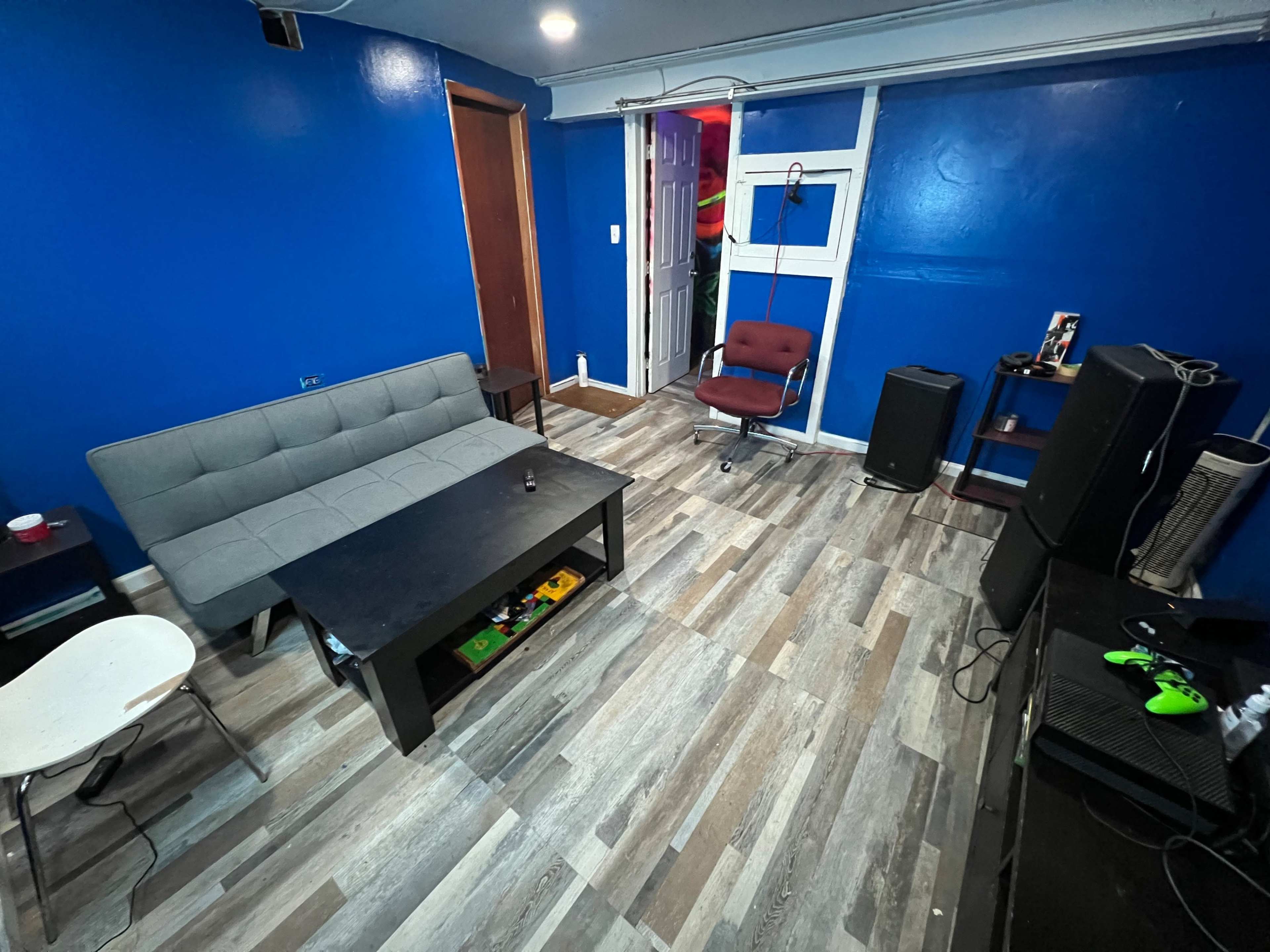 A room with blue walls, featuring a gray sofa, a black coffee table, a red chair, and various electronic devices arranged around the space.