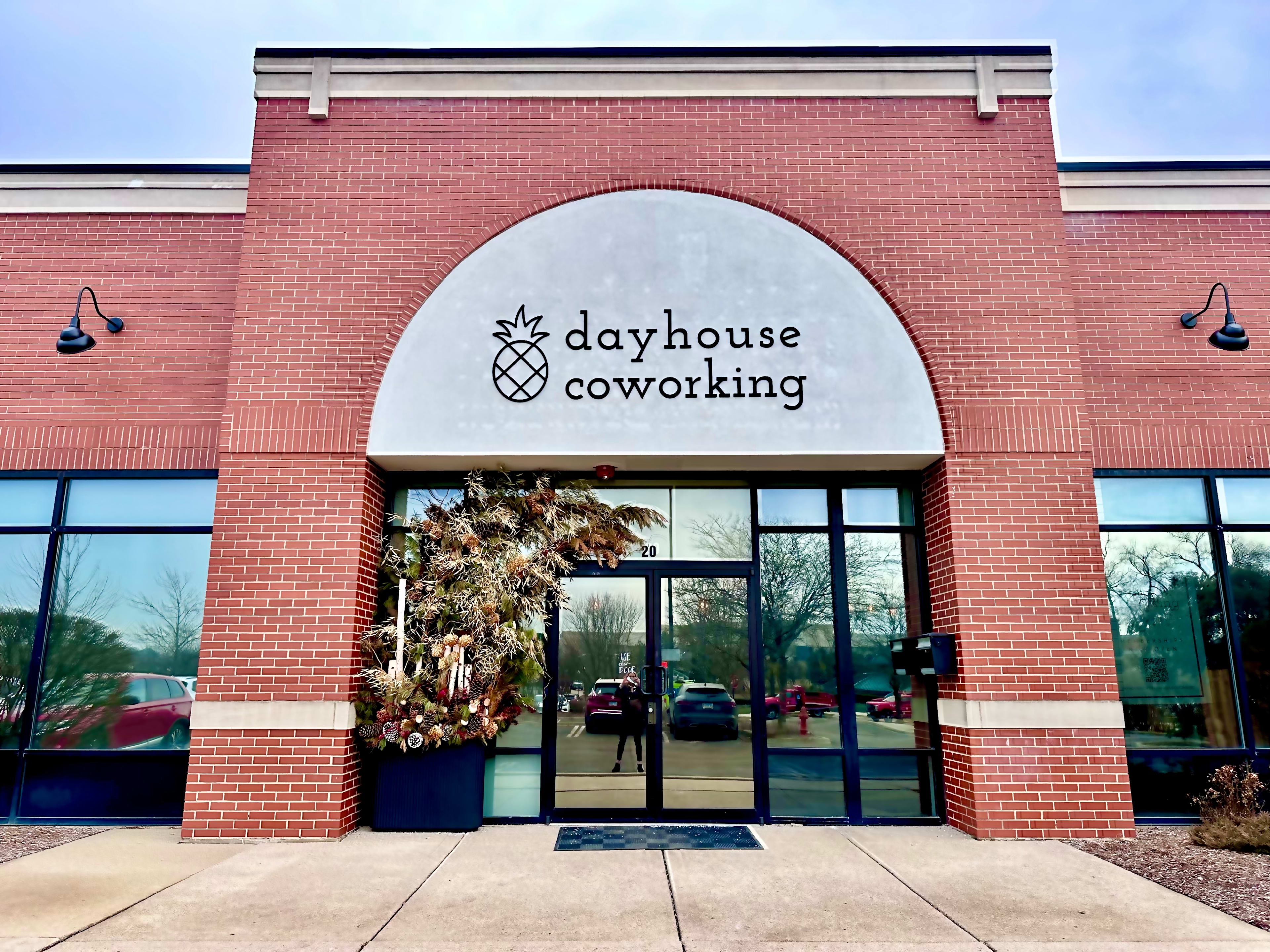 The image shows the exterior of a coworking space named "dayhouse coworking," featuring a prominent sign and a decorative arrangement near the entrance.