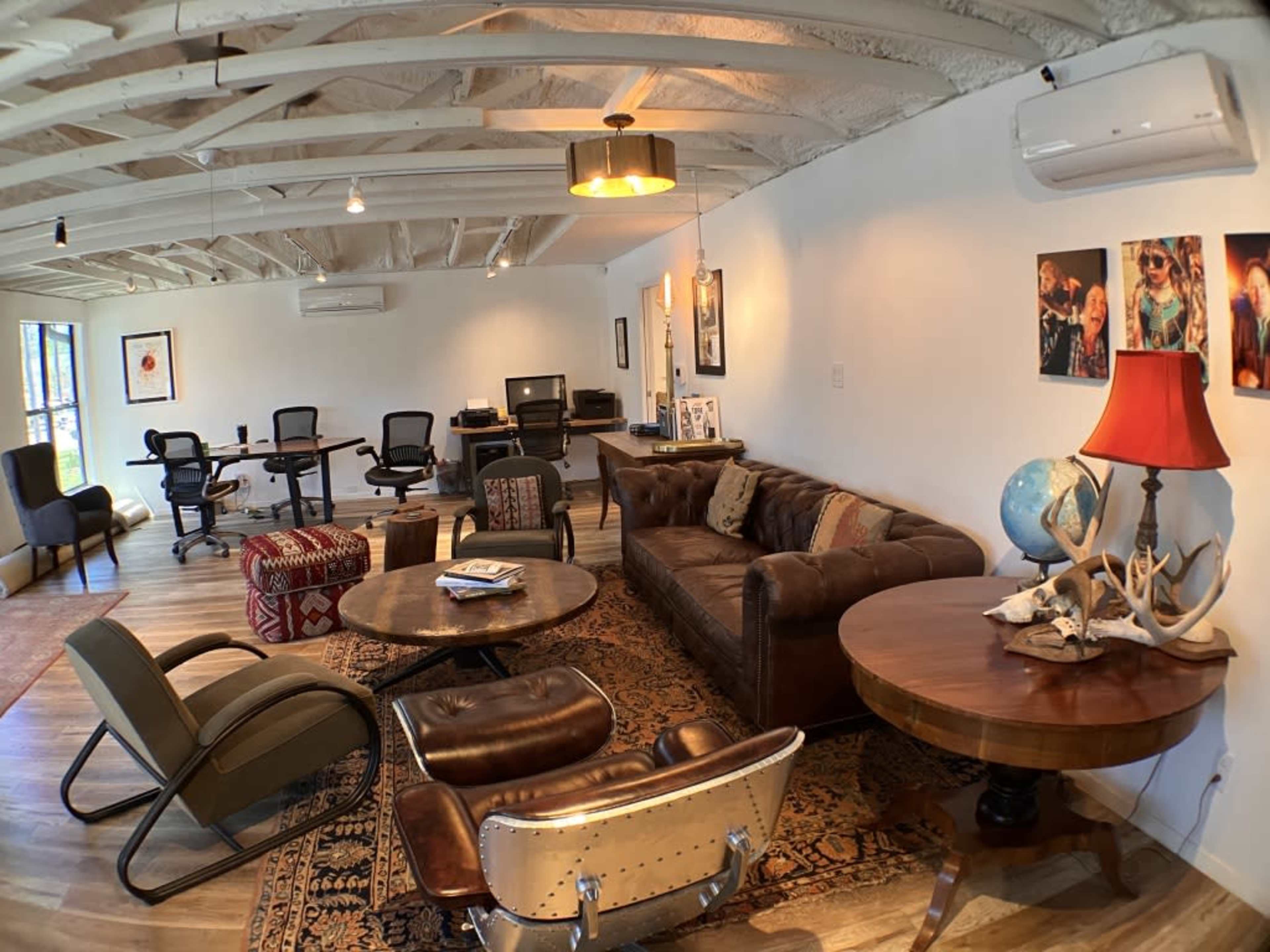 The image shows a spacious office area featuring a mix of seating options, including a leather sofa and various chairs, along with several tables and open workspaces.