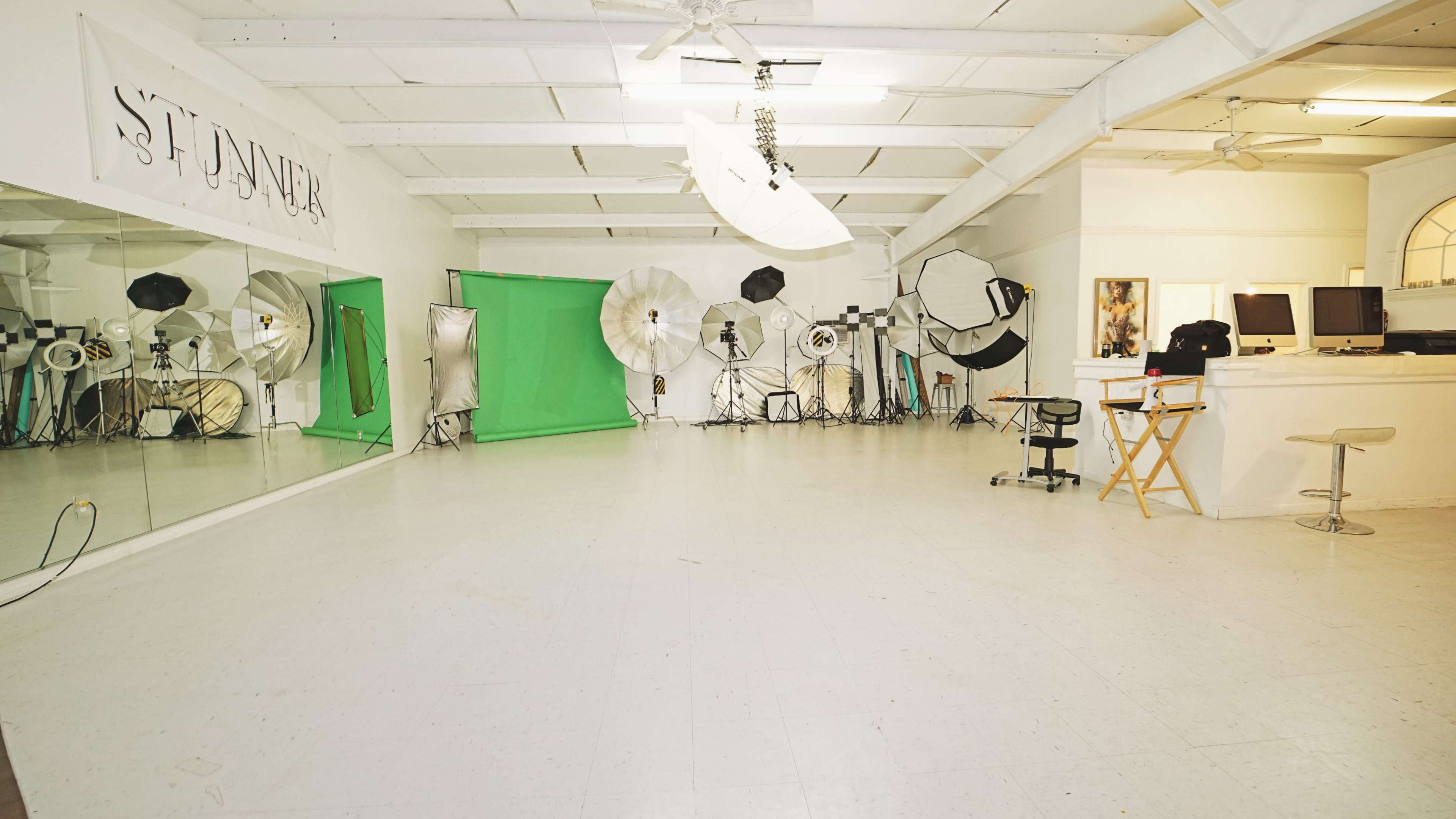 A spacious photography studio equipped with various lighting equipment, a green screen, and a large mirror.