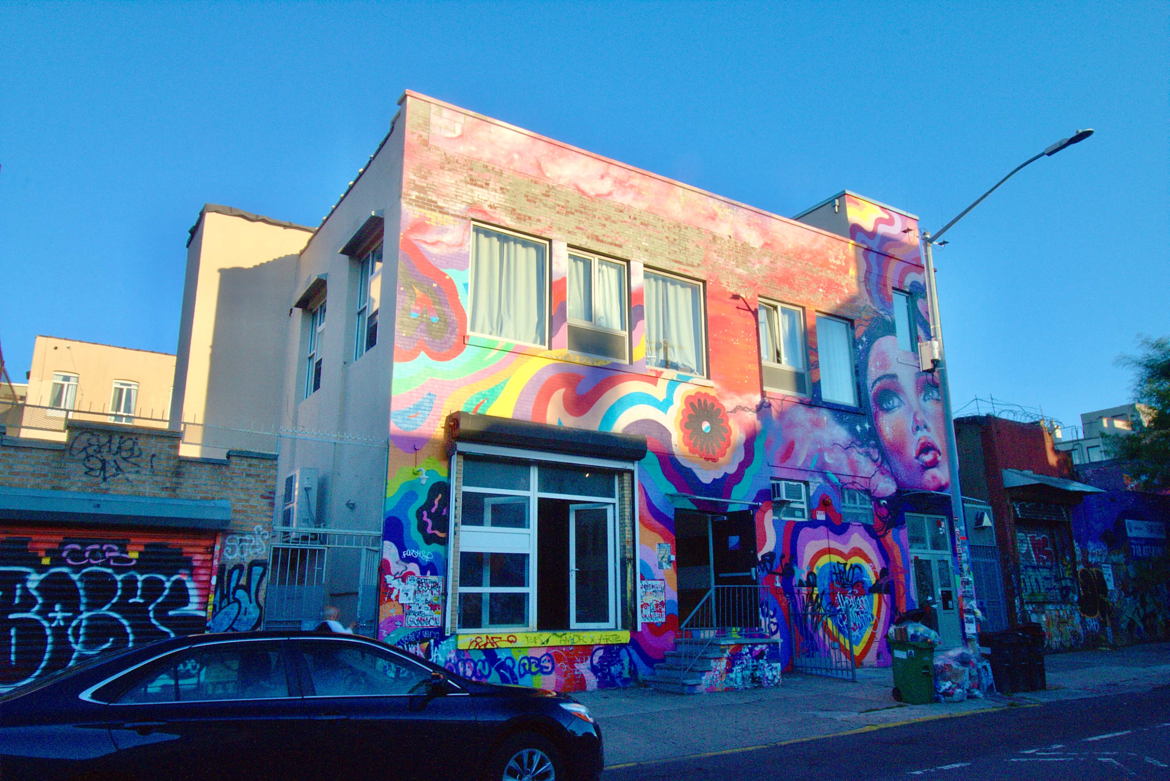A multi-story building features a vibrant mural on its facade, showcasing colorful abstract designs and portraits.