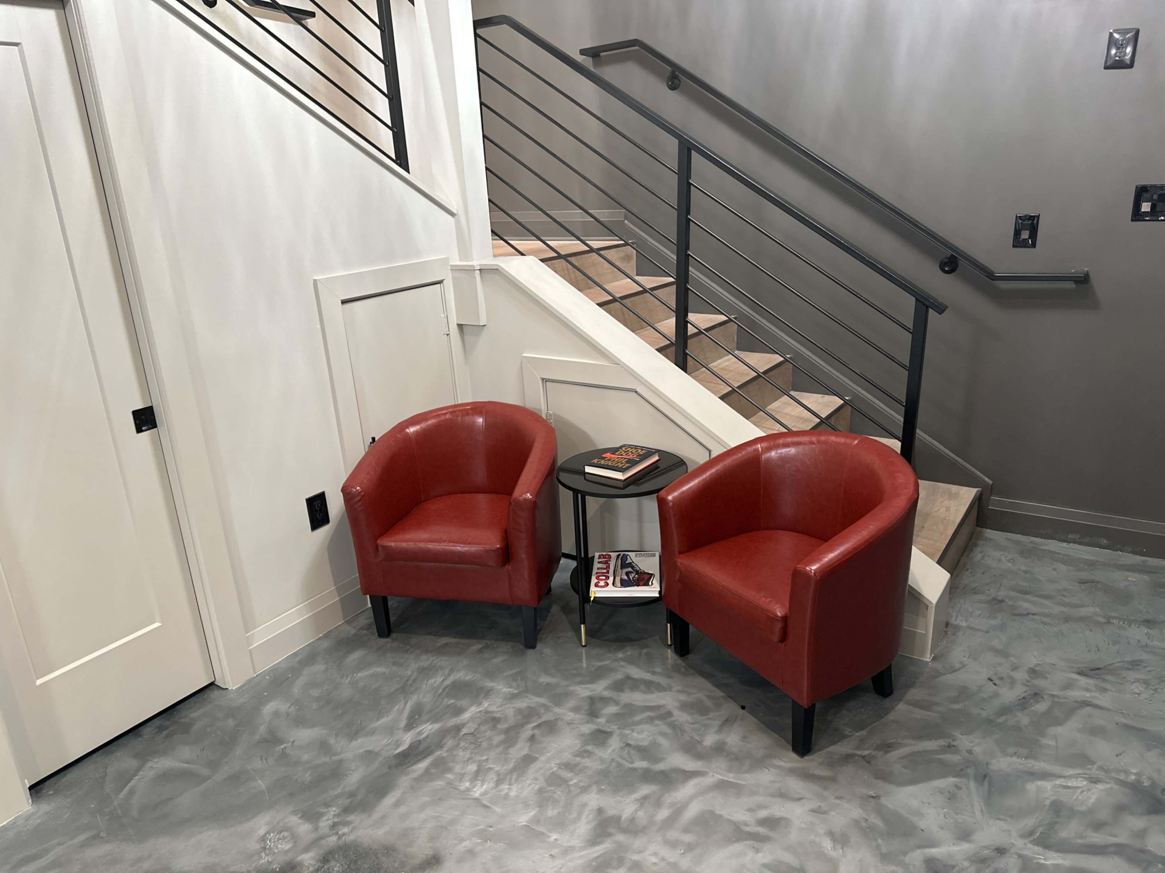 Two red armchairs flanking a small round table at the foot of a staircase in a modern interior.