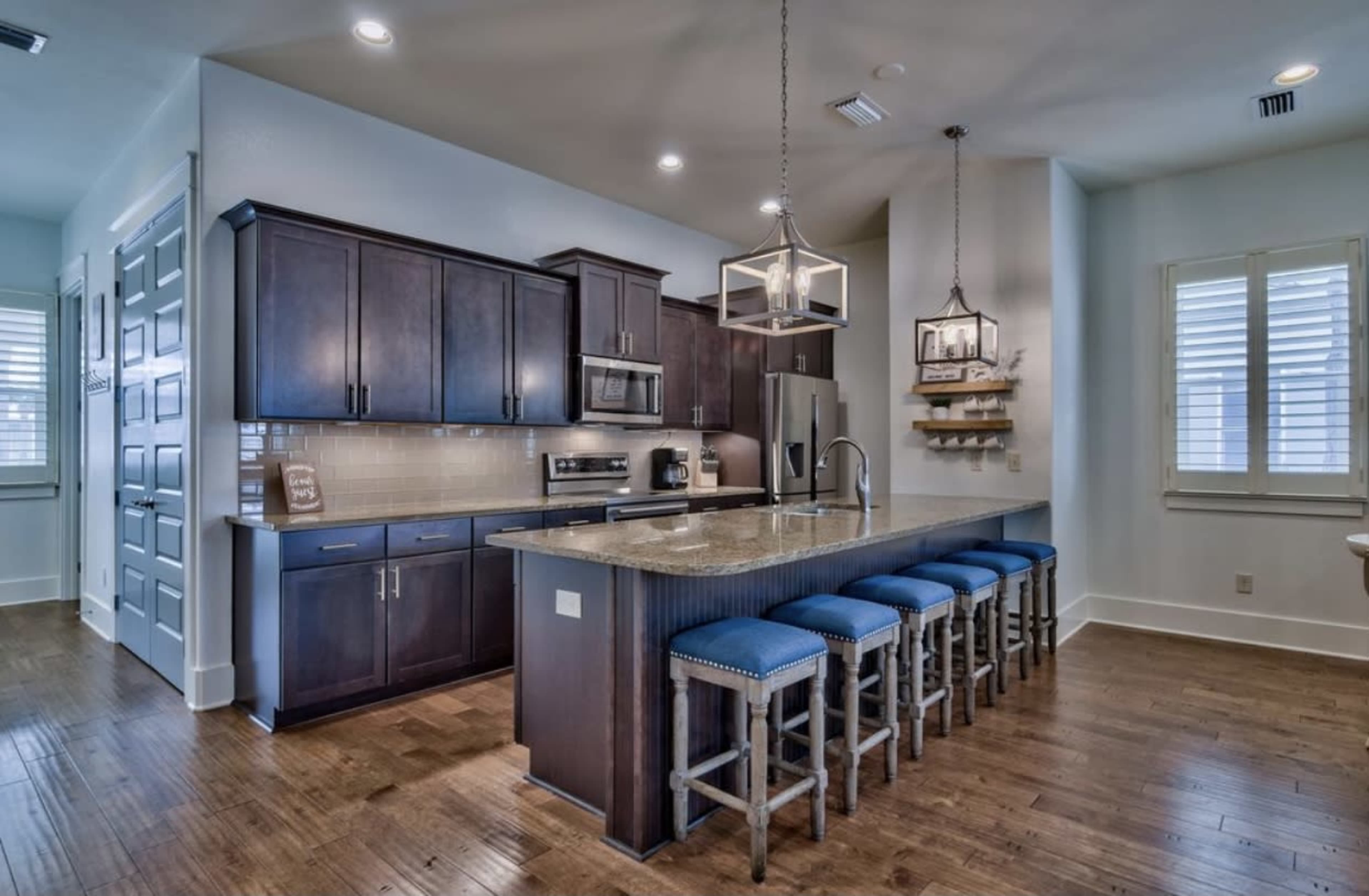 A modern kitchen with dark wooden cabinets, a large granite countertop, and blue upholstered counter stools arranged in front of it.