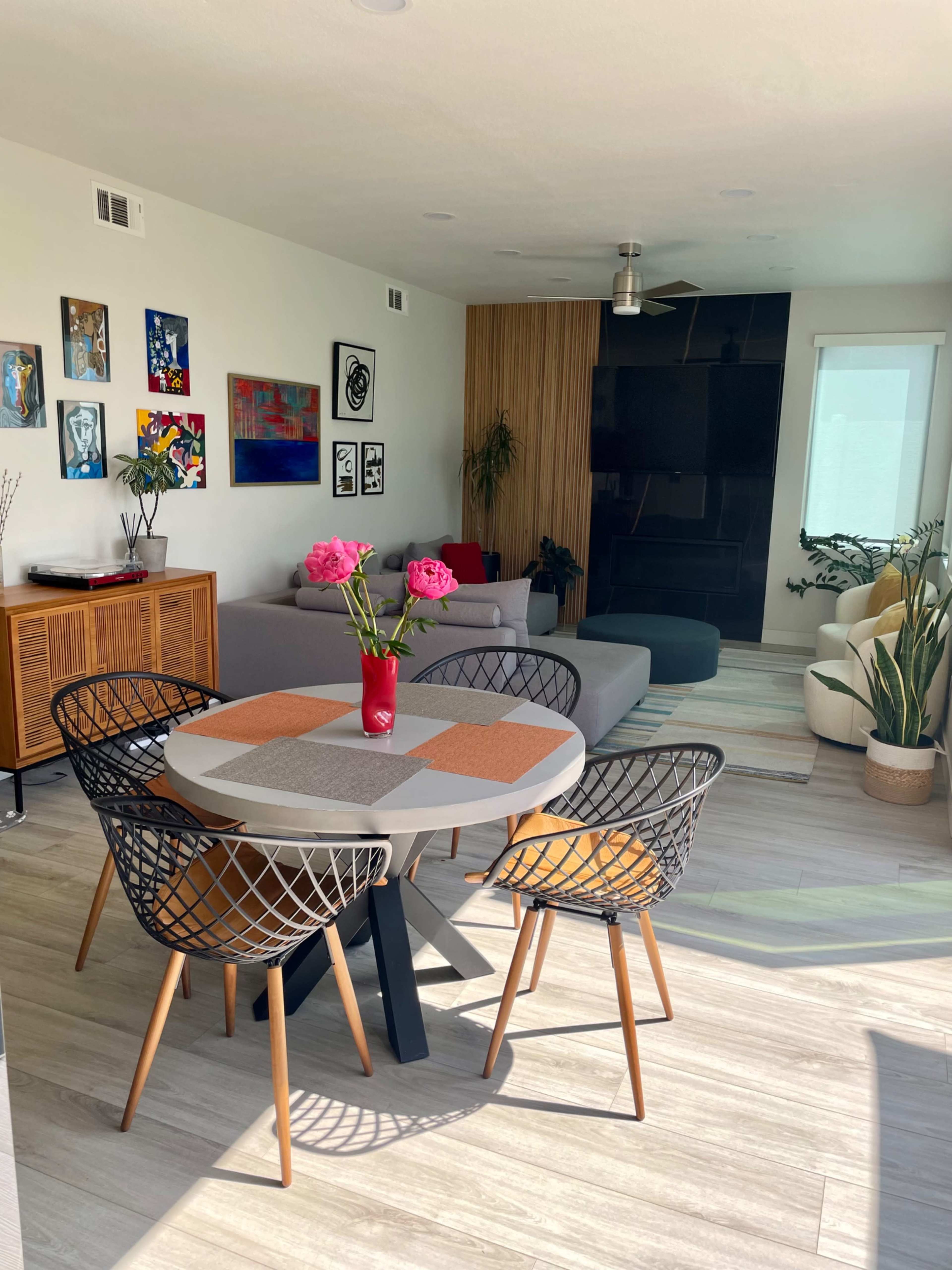 A modern living space features a round dining table surrounded by four chairs, with a sofa in the background and decorative artwork on the walls.