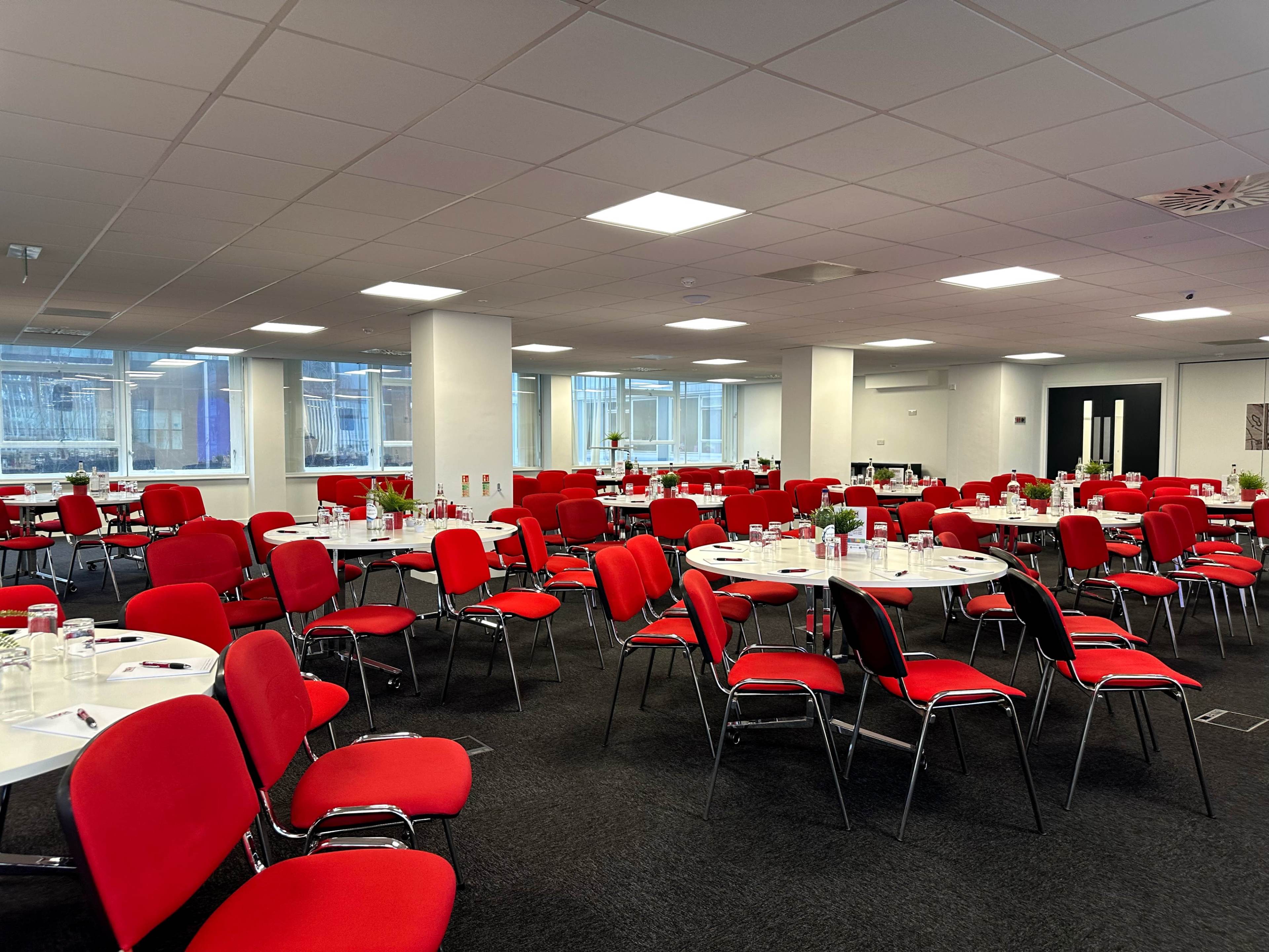 A conference room set up with round tables surrounded by red chairs, ready for an event.