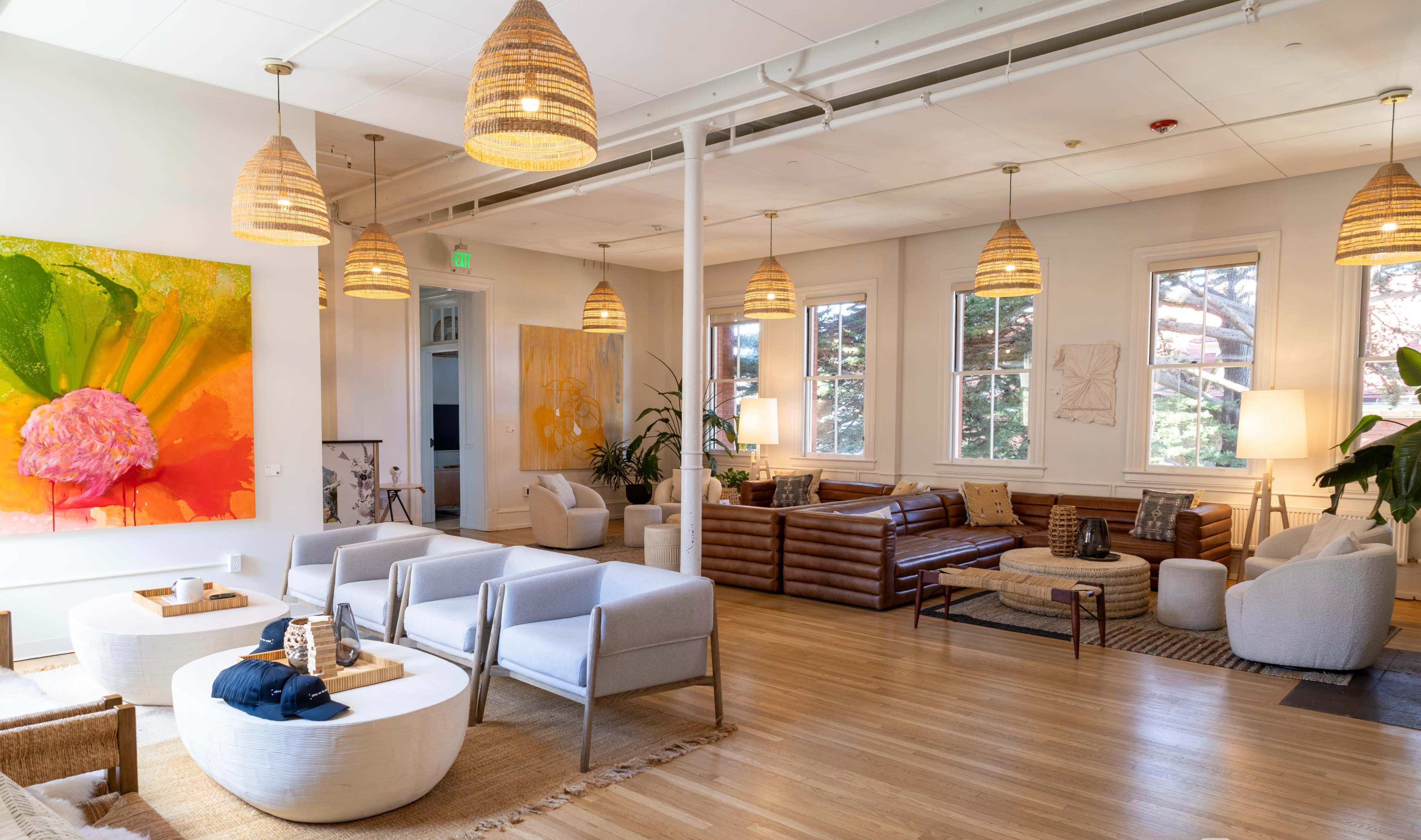 The image shows a bright, modern lounge area with comfortable seating, large windows, and decorative pendant lights.