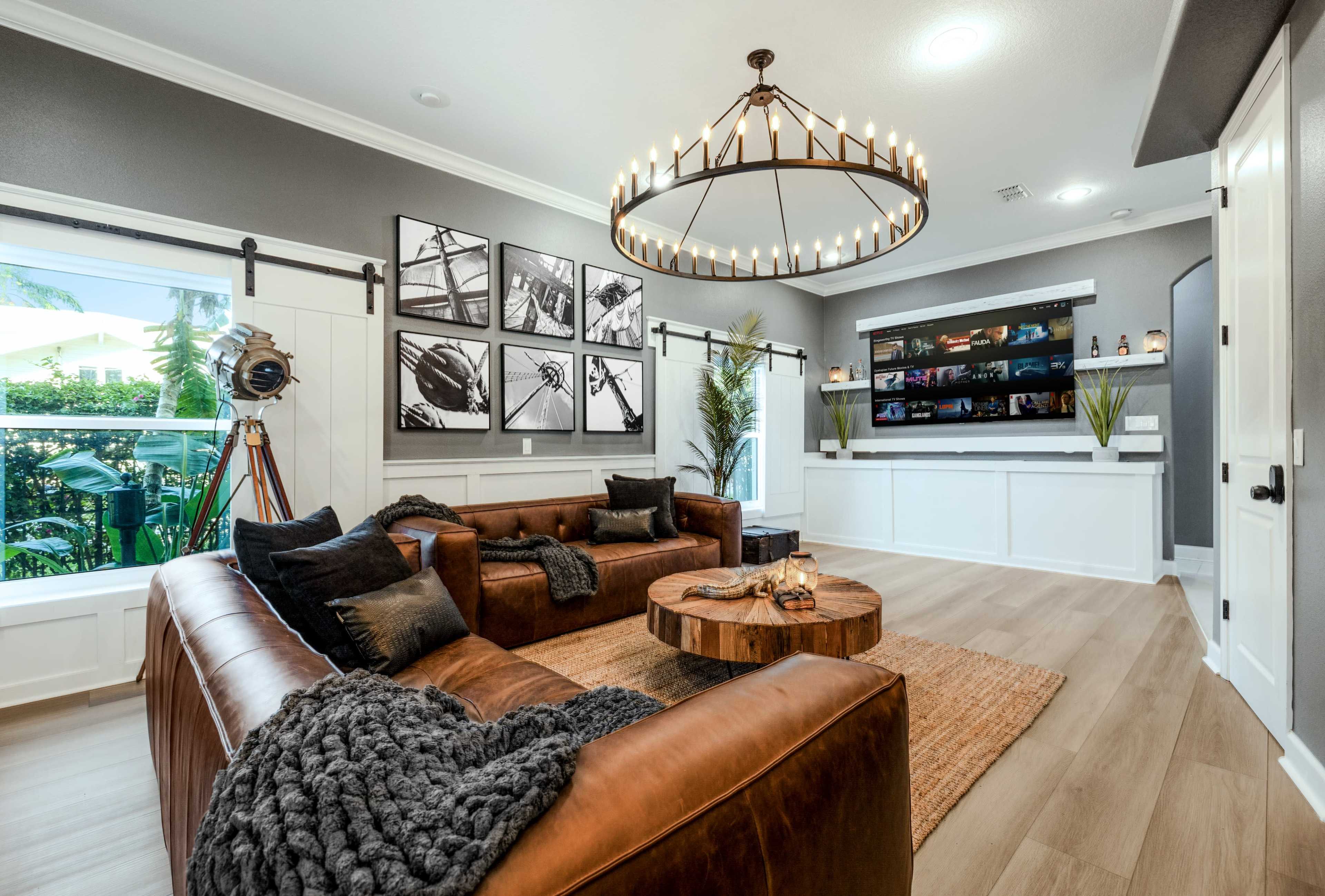 The image shows a modern living room with two brown leather sofas, a circular chandelier, and a wall-mounted display shelf featuring various decor items.