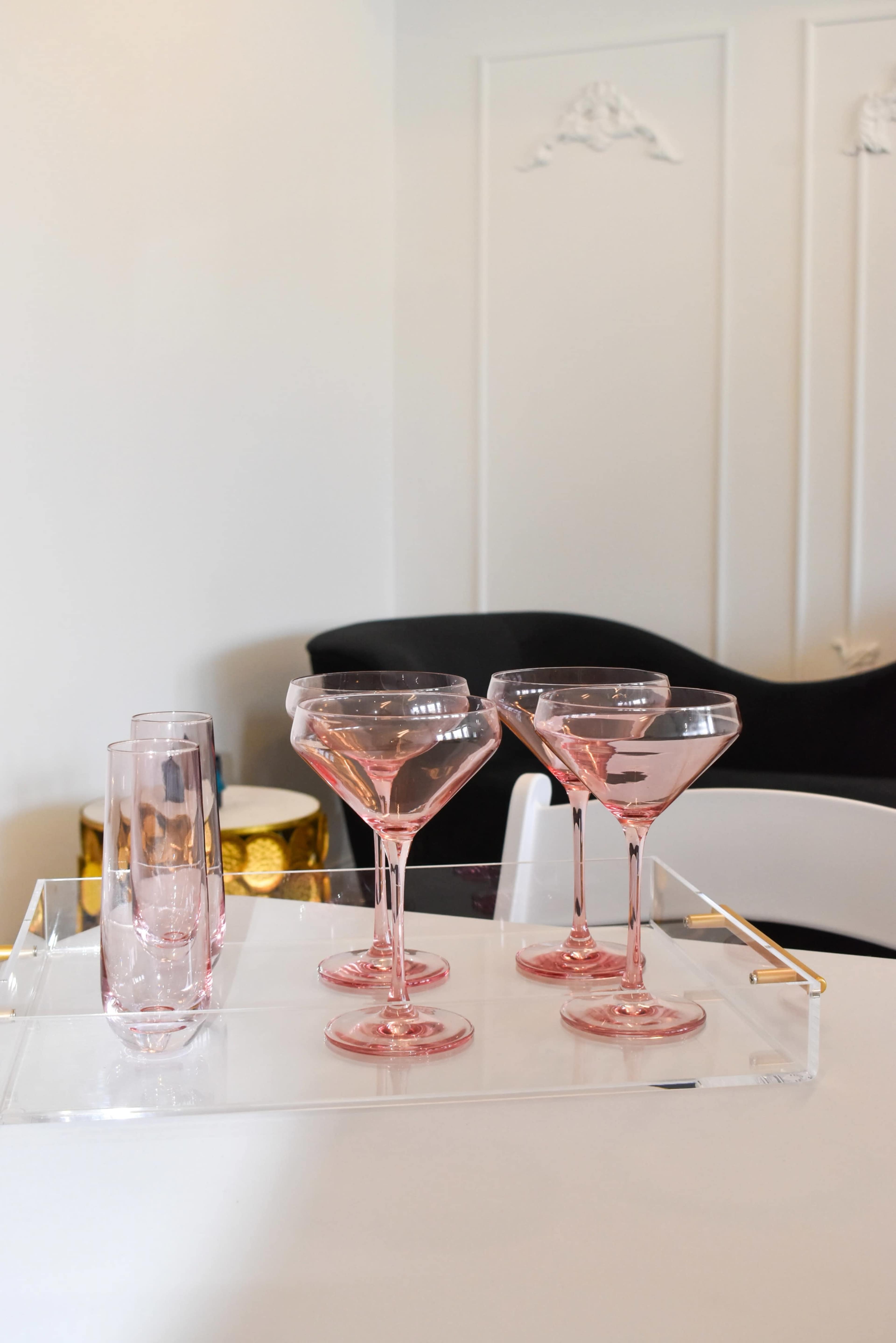 A set of pink glassware is arranged on a tray beside a black chair and a decorative drum.