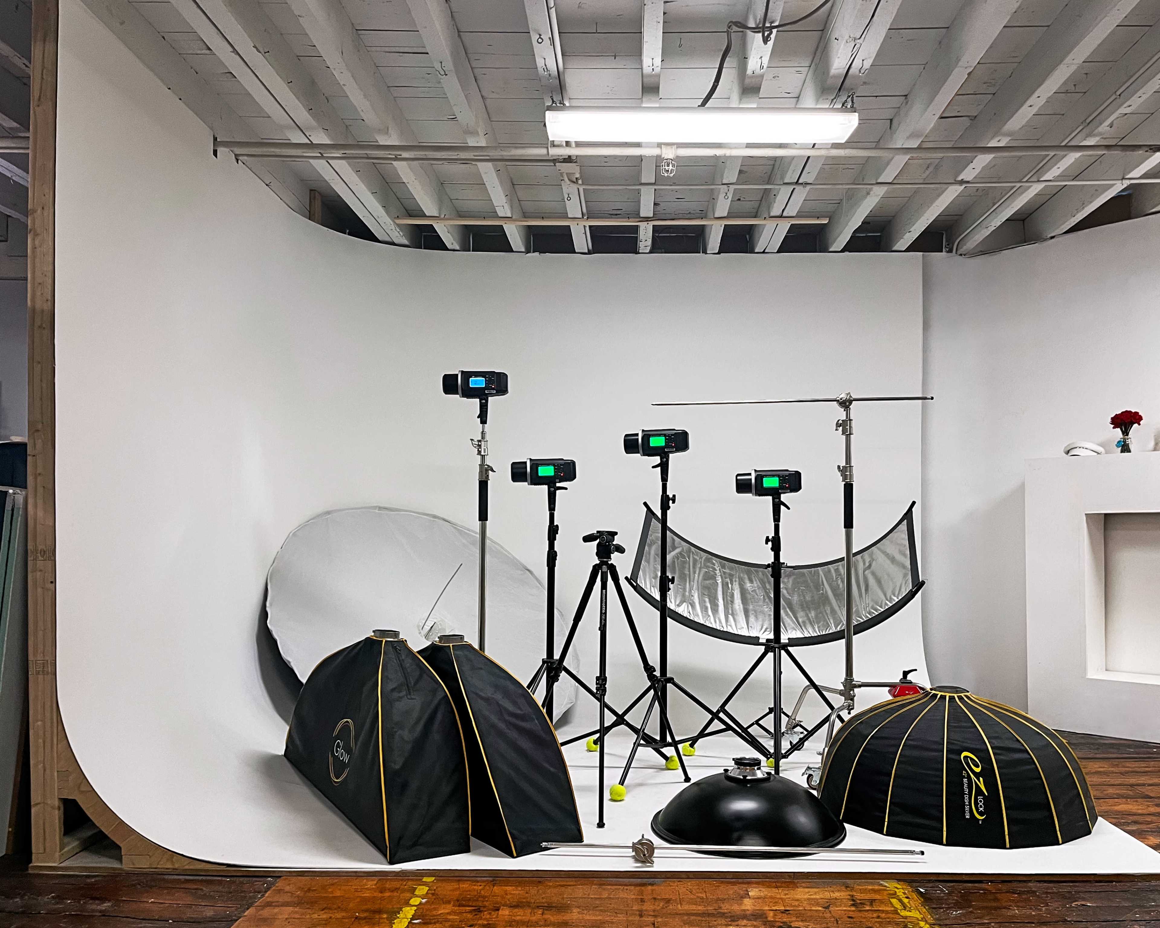 The image shows a photography studio setup with multiple light stands, softboxes, and a large white backdrop.
