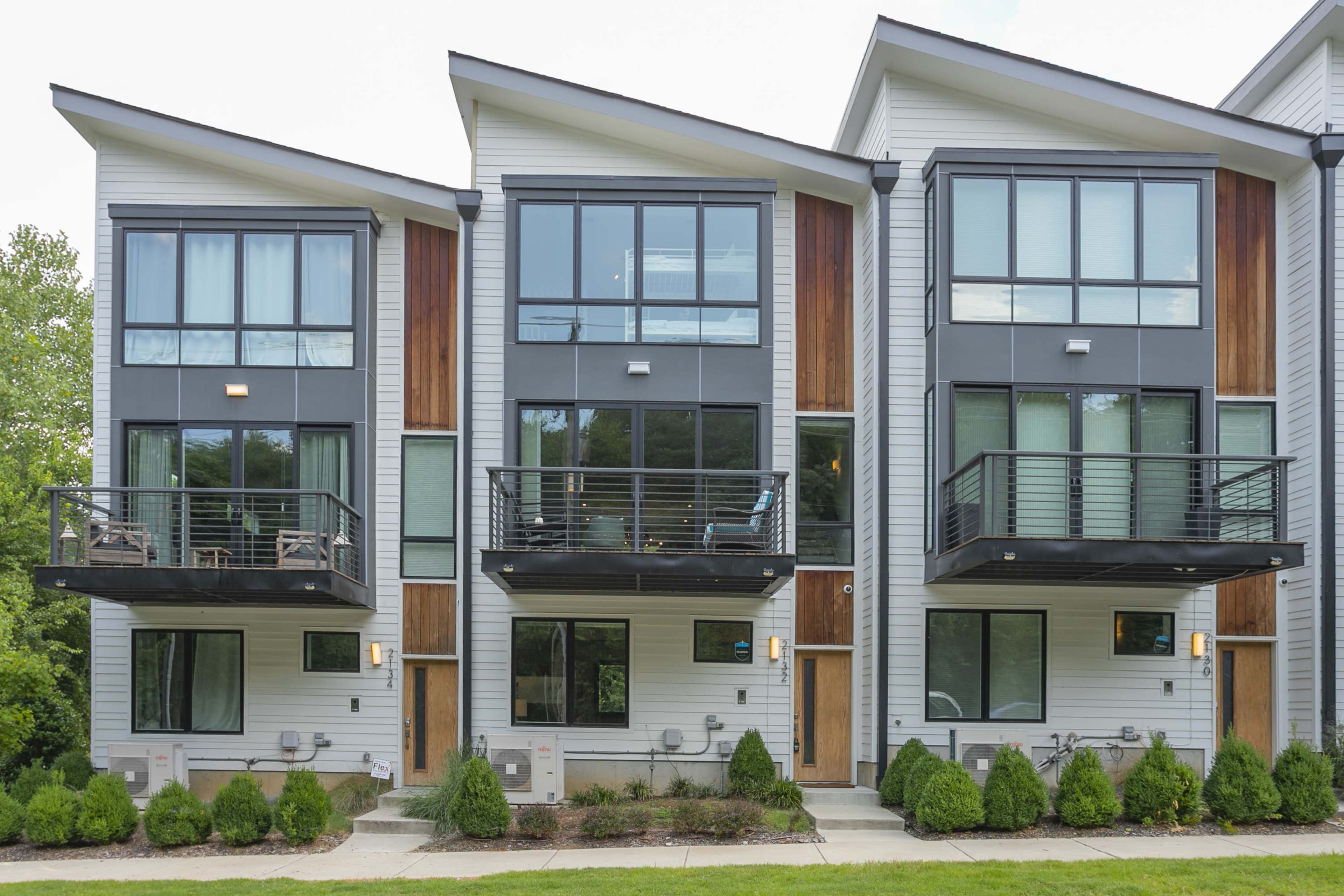 A row of modern townhouses with large windows and balconies, set in a landscaped area.