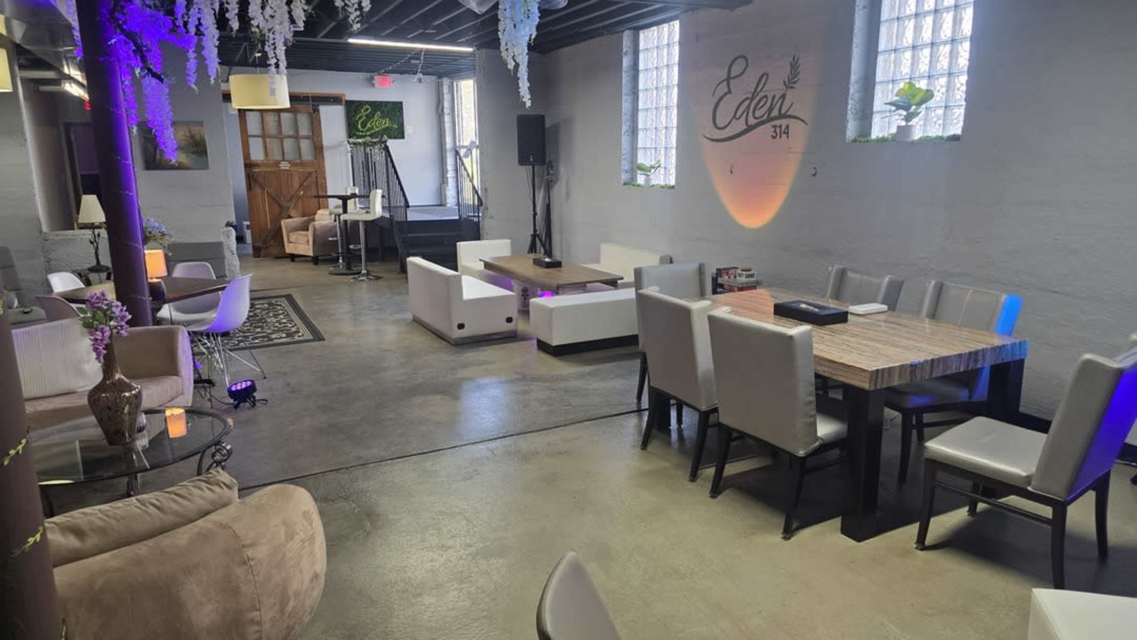 The image shows a spacious, modern event space with a mix of seating arrangements, including lounge chairs and dining tables, illuminated by soft lighting.