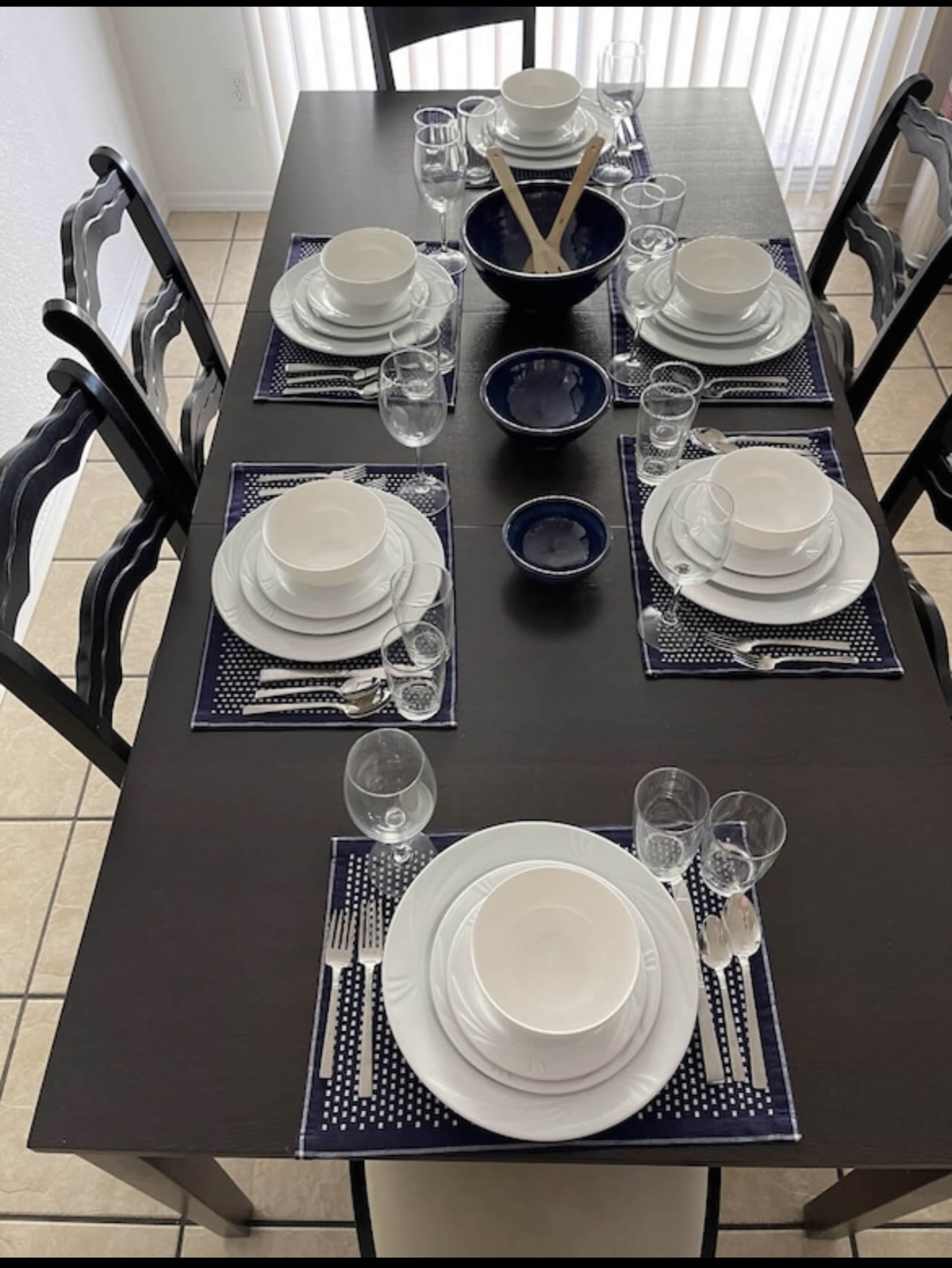 A dining table is set with white dinnerware, glassware, and navy blue placemats arranged for eight people.