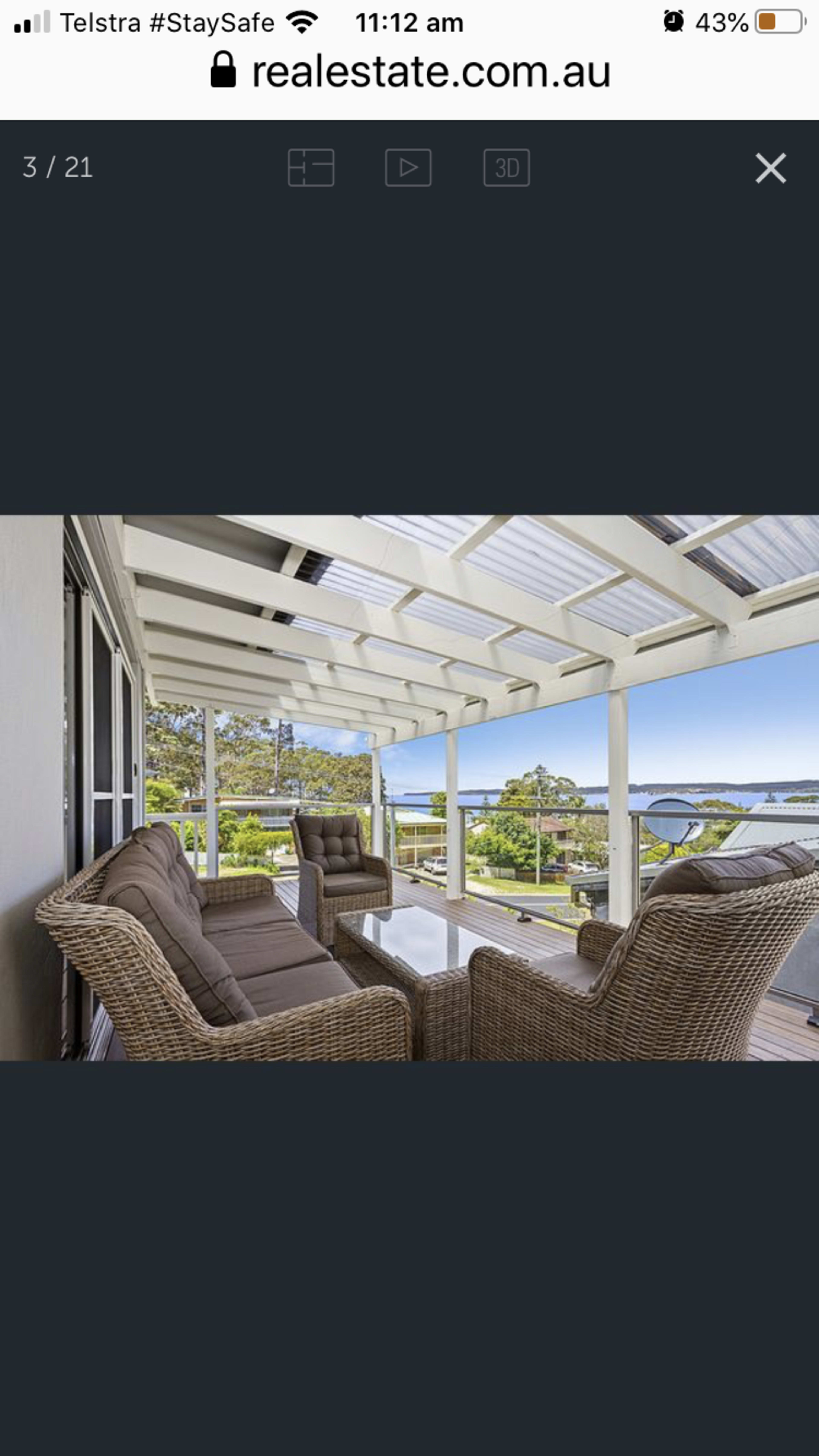 A covered patio features wicker furniture and a clear view of the landscape beyond.