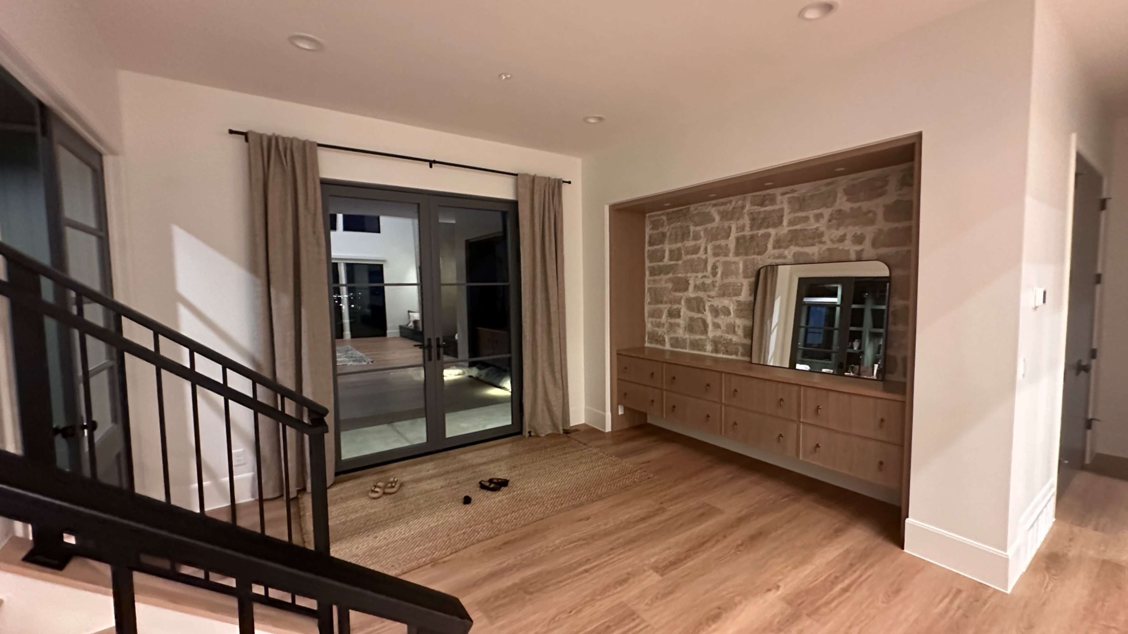 A well-lit entryway with a staircase, a stone feature wall, a large mirror above a wooden console, and glass doors leading to an outdoor area.