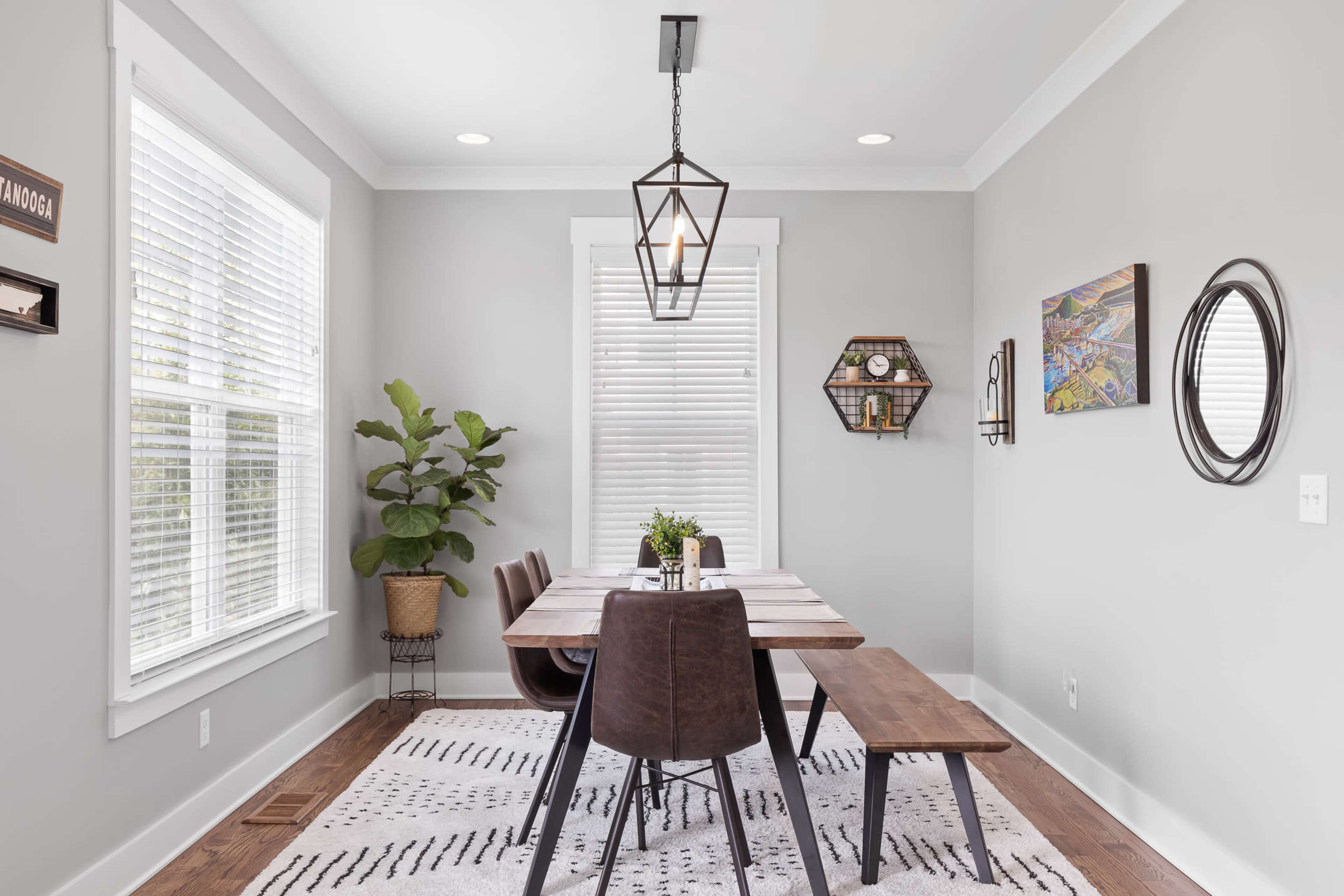 A modern dining area features a wooden table surrounded by dark chairs, with a large pendant light overhead and decorative elements on the walls.