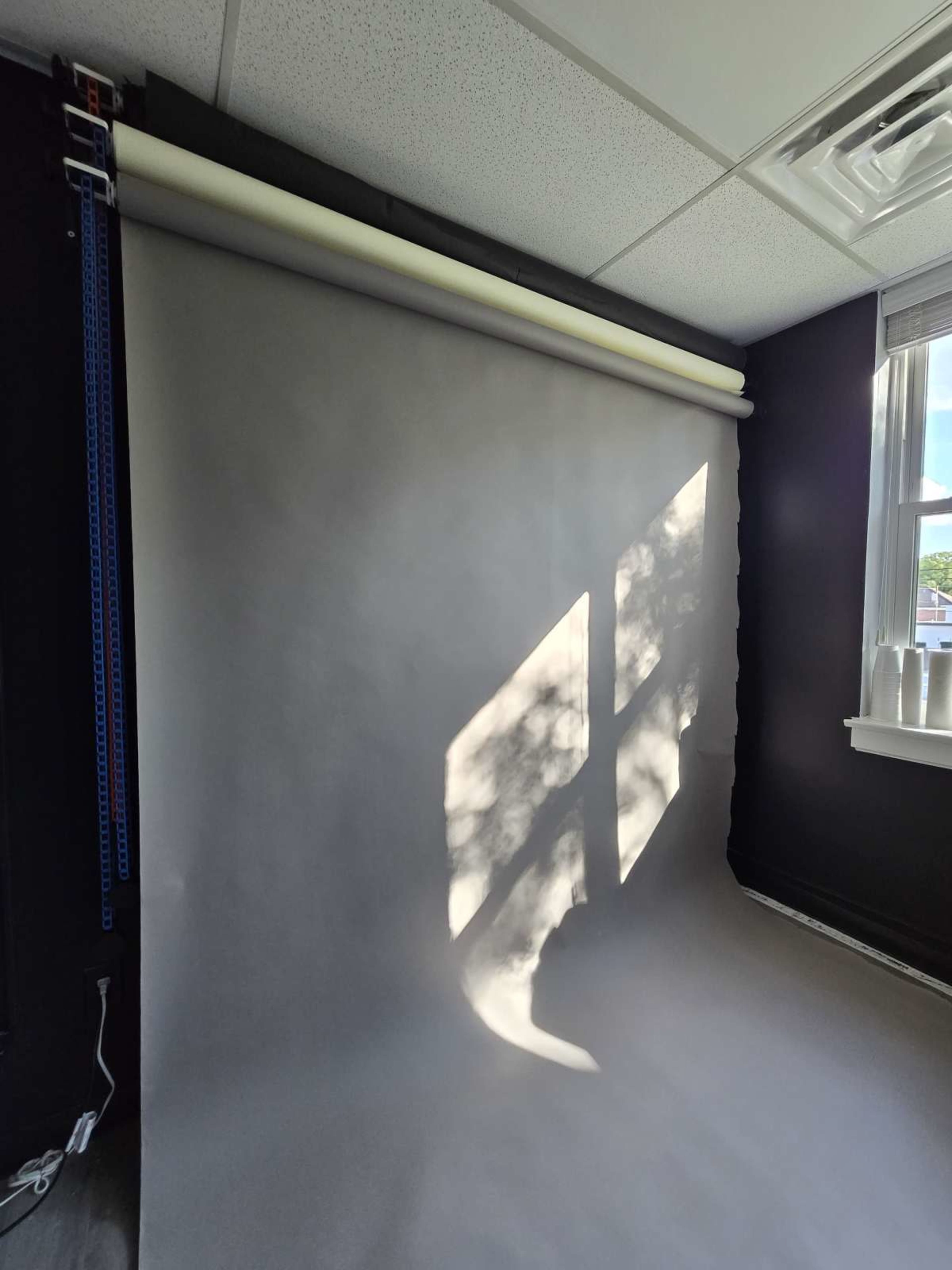 A photography studio with a gray backdrop and sunlight casting a shadow of a window on the wall.