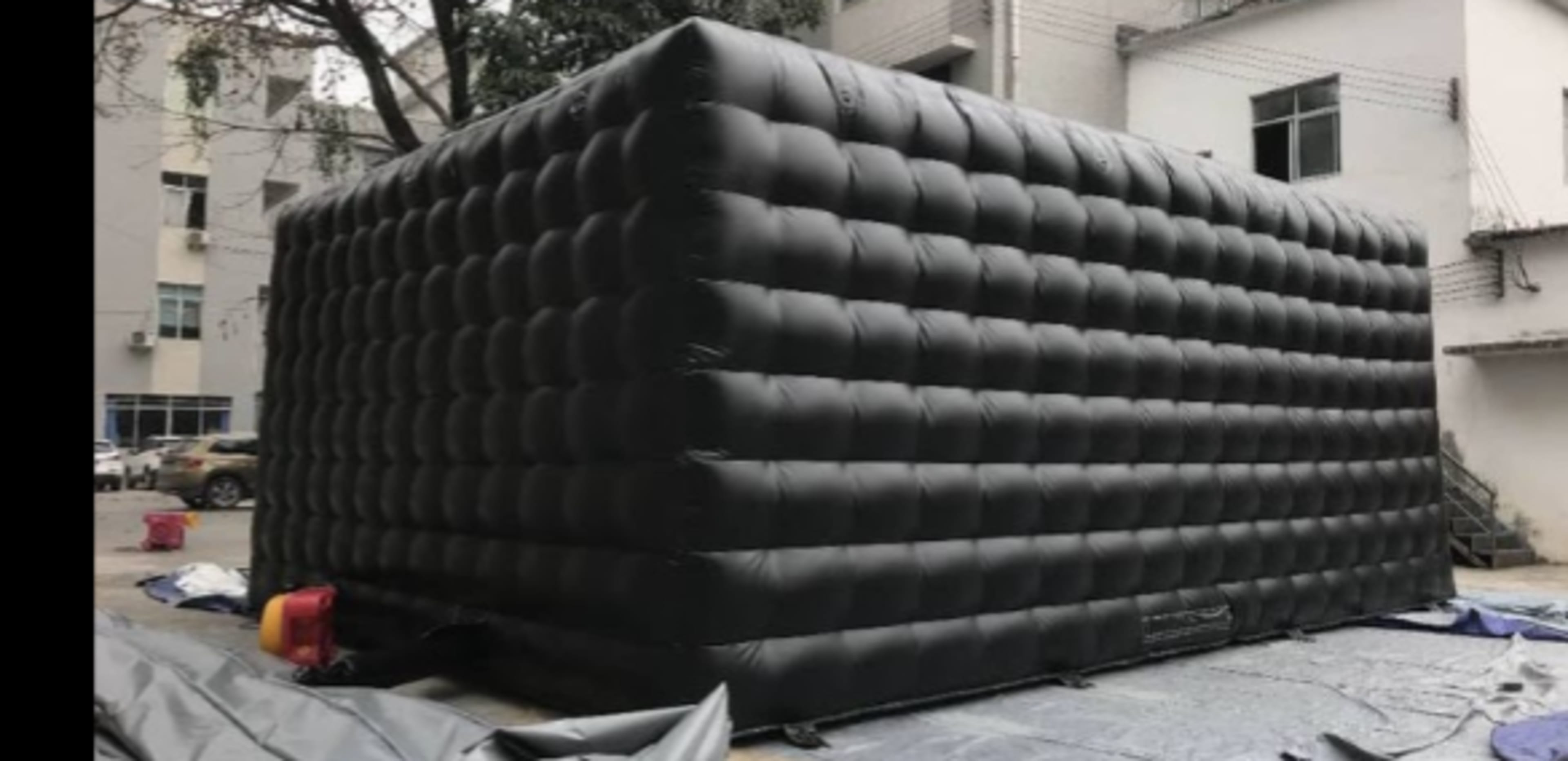 A large, inflatable black structure with a quilted surface, set up in an outdoor area near buildings.